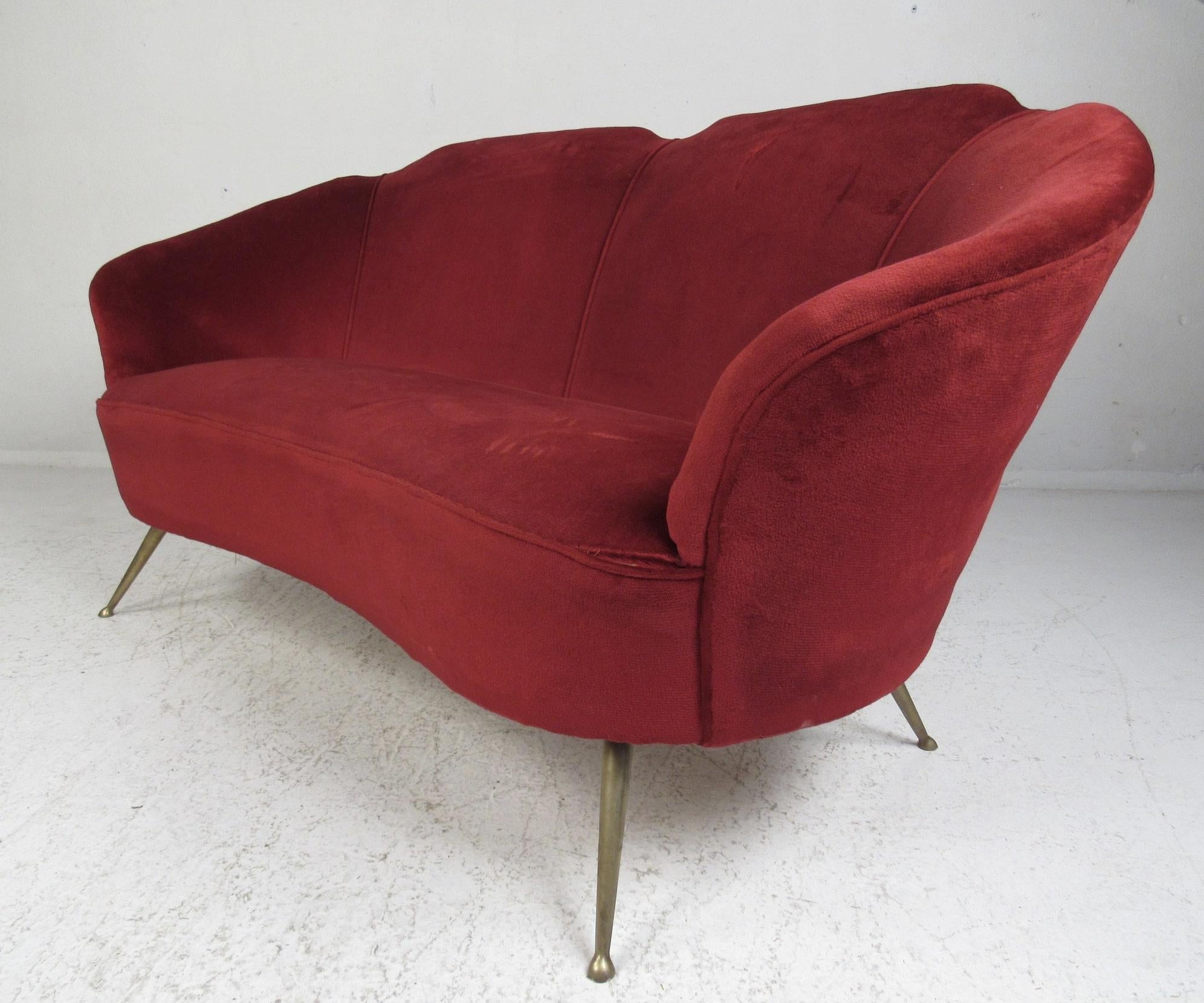 Stunning vintage modern living room loveseat. The red velour upholstery and brass drumstick legs are sure to make an impression in any seating arrangement. A sleek design that features shell barrel backrests and thickly padded seats providing plenty