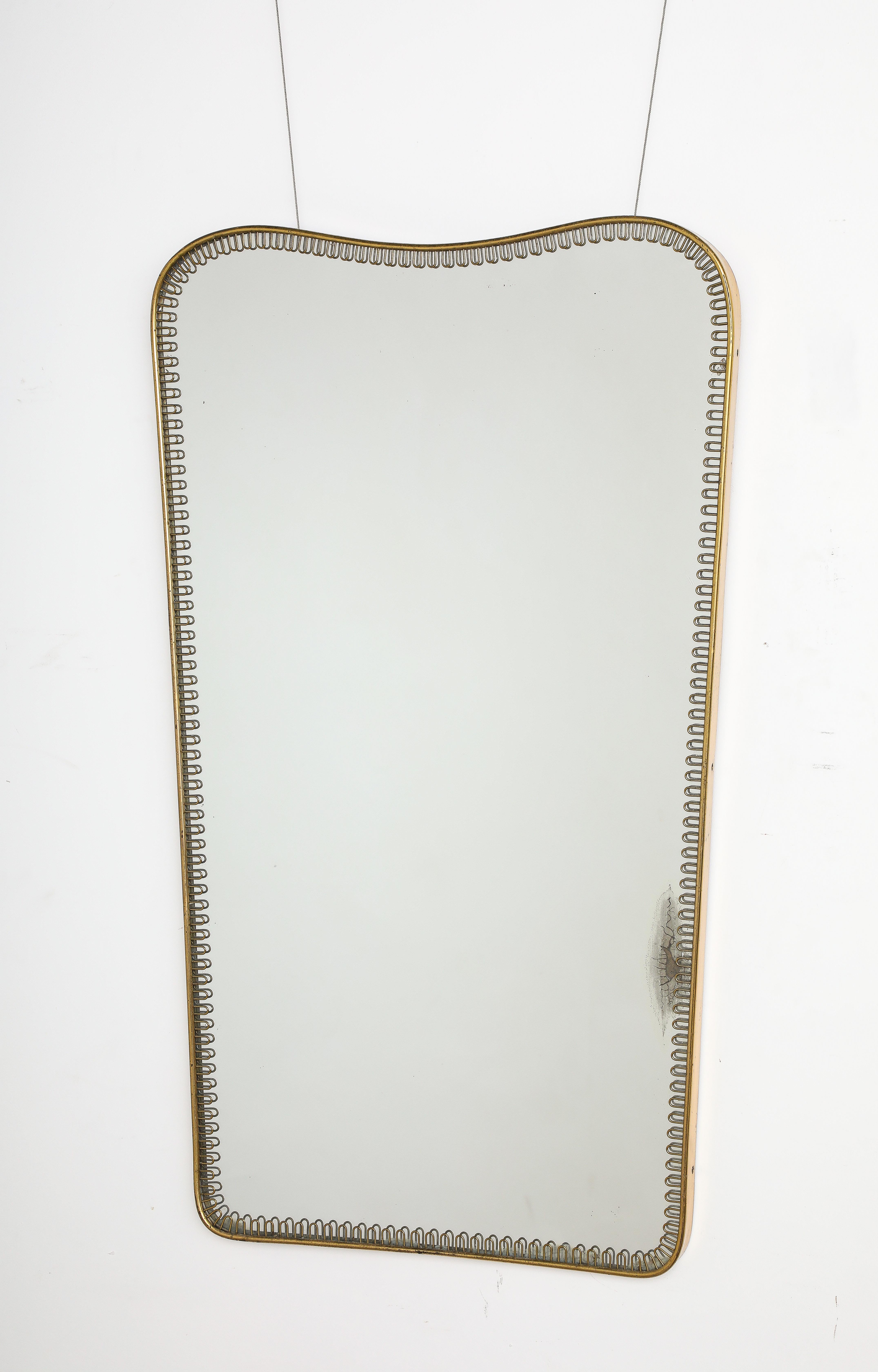 A rare and elegant brass framed mirror attribute to designer Gio Ponti, the crest is shaped and tapers downward to a straight side and base.  The whole mirror plate is surrounded with brass scroll motif bordering the outer brass molding.  The brass