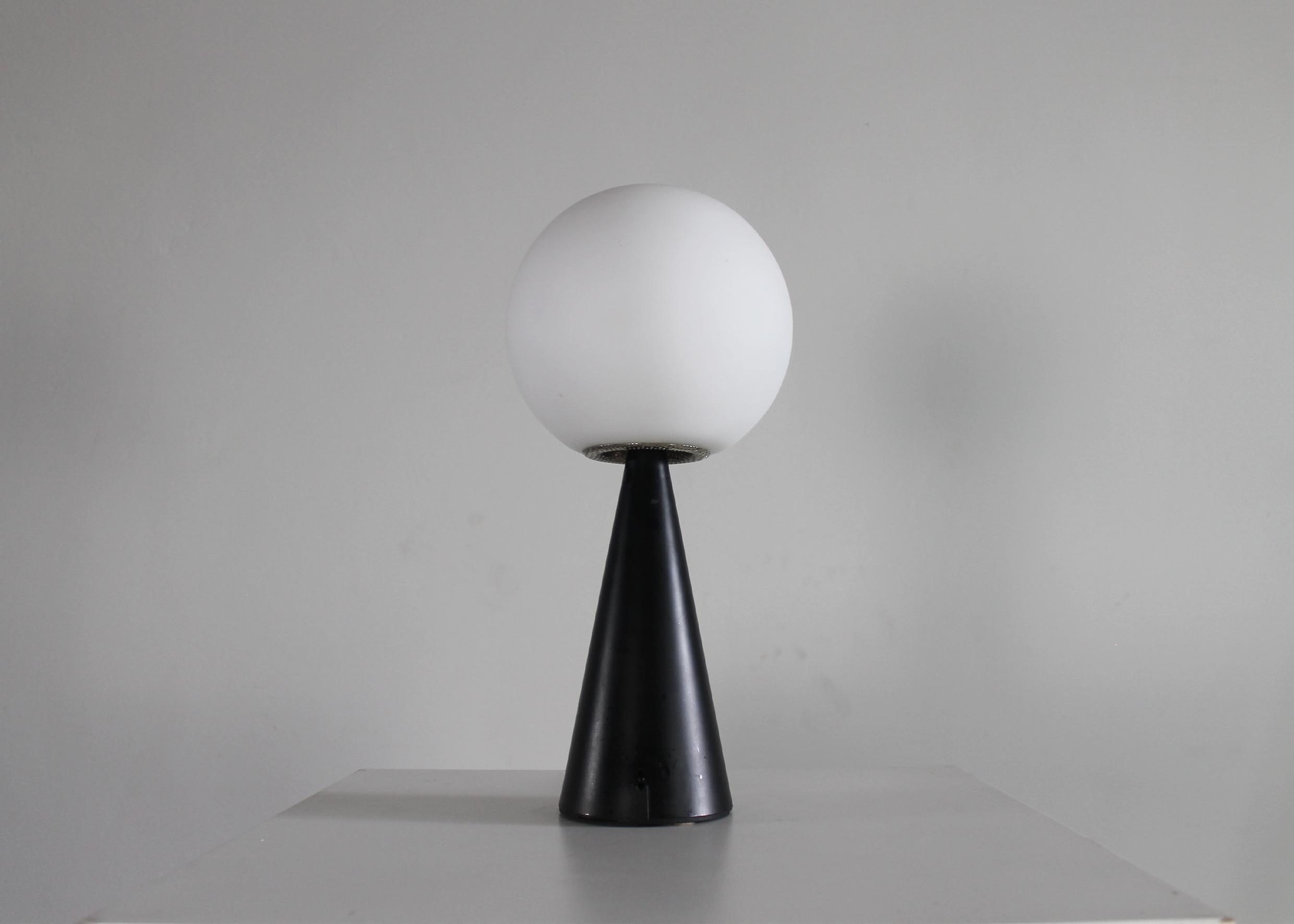 Lampe de table Bilia avec une base conique en métal laqué noir reliée à un abat-jour sphérique en verre opalin soufflé.

Il s'agit d'une lampe emblématique basée sur deux formes essentielles qui, mélangées, recréent une composition