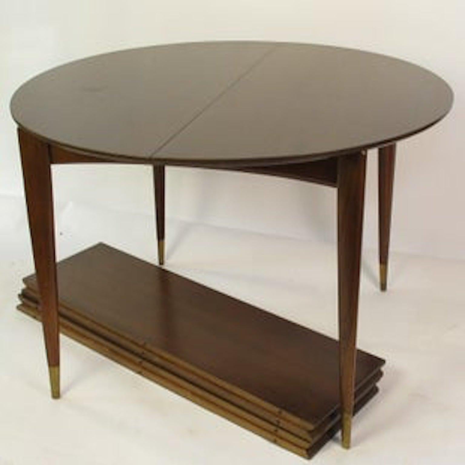 Midcentury walnut dining table made in America by Singer and Sons. Beautiful tapered legs each leg has a brass shoe which need to be refinished. The size is perfect for small dining room. Four individual leaves can be inserted extending length to