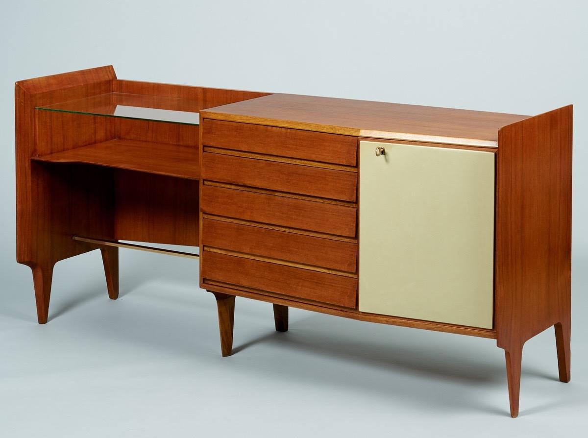 Gio Ponti (1891 - 1979) 

An exceptional and rare asymmetrical credenza by modernist master Gio Ponti, in mahogany with five drawers angled subtly outwards, a glass writing desk, polished brass hardware, and the original cream-colored skai door with