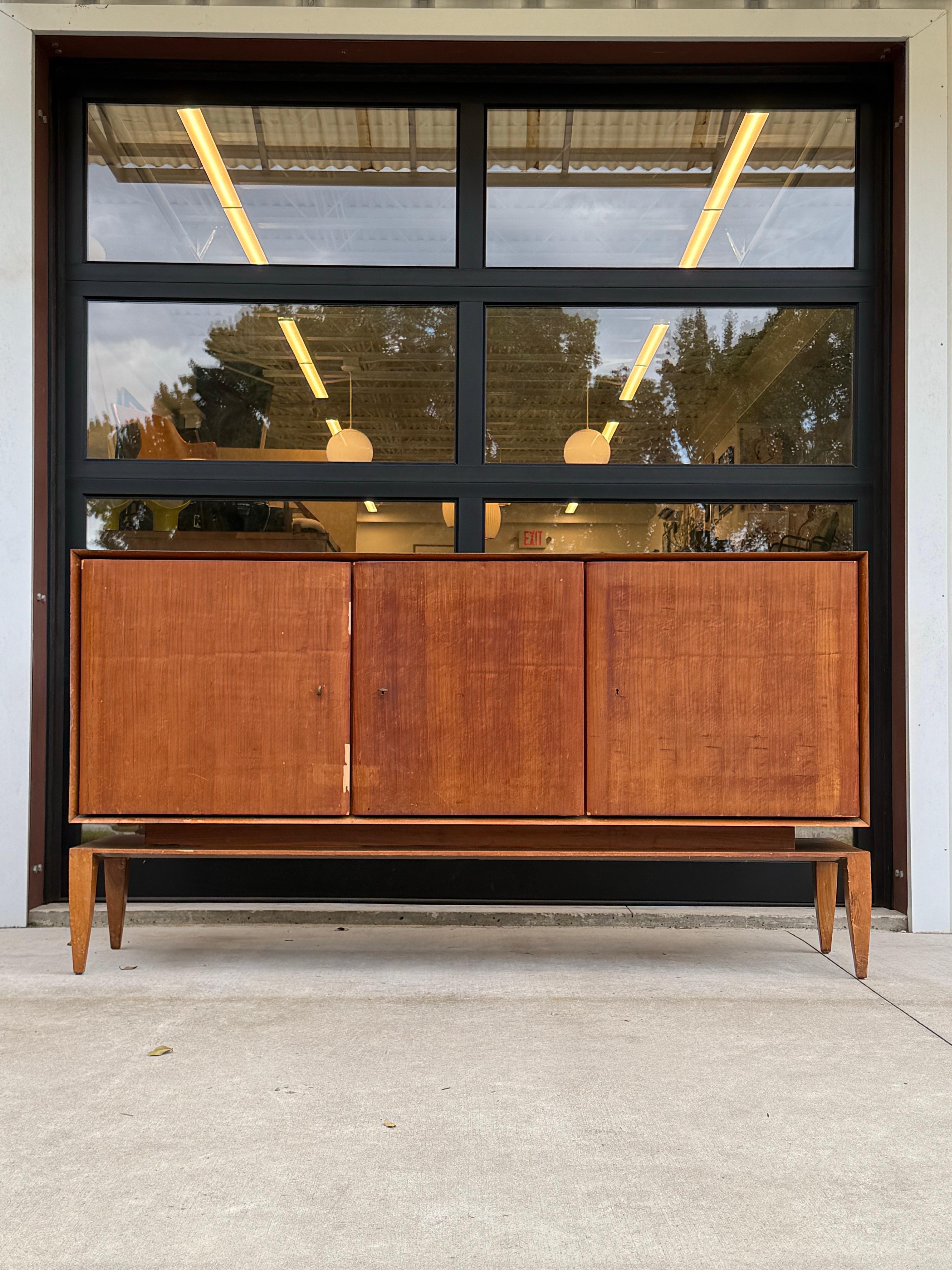 A stunning mid-century modern credenza by the legendary Italian designer Gio Ponti, crafted circa 1950–1951 for M. Singer & Sons. This exquisite Model 2160 features a sleek, low-profile walnut veneer body with three symmetrical flush doors subtle