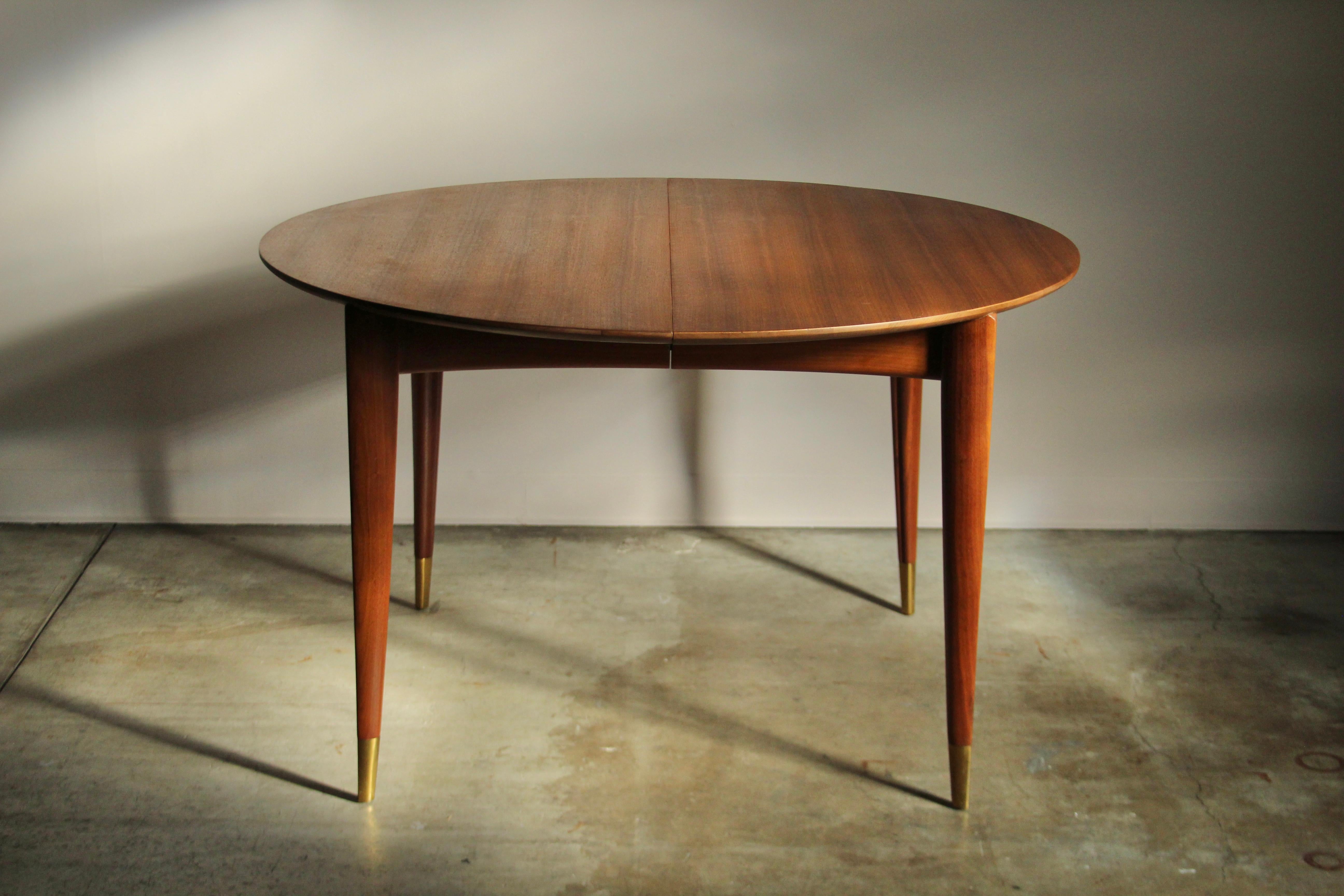 Gio Ponti for Singer & Sons 'Model 2135' dining table with two leaves. This example features a sculpted, solid walnut base with brass cape feet, and a ribbon mahogany top. The round table may be expanded to add one of two additional 14