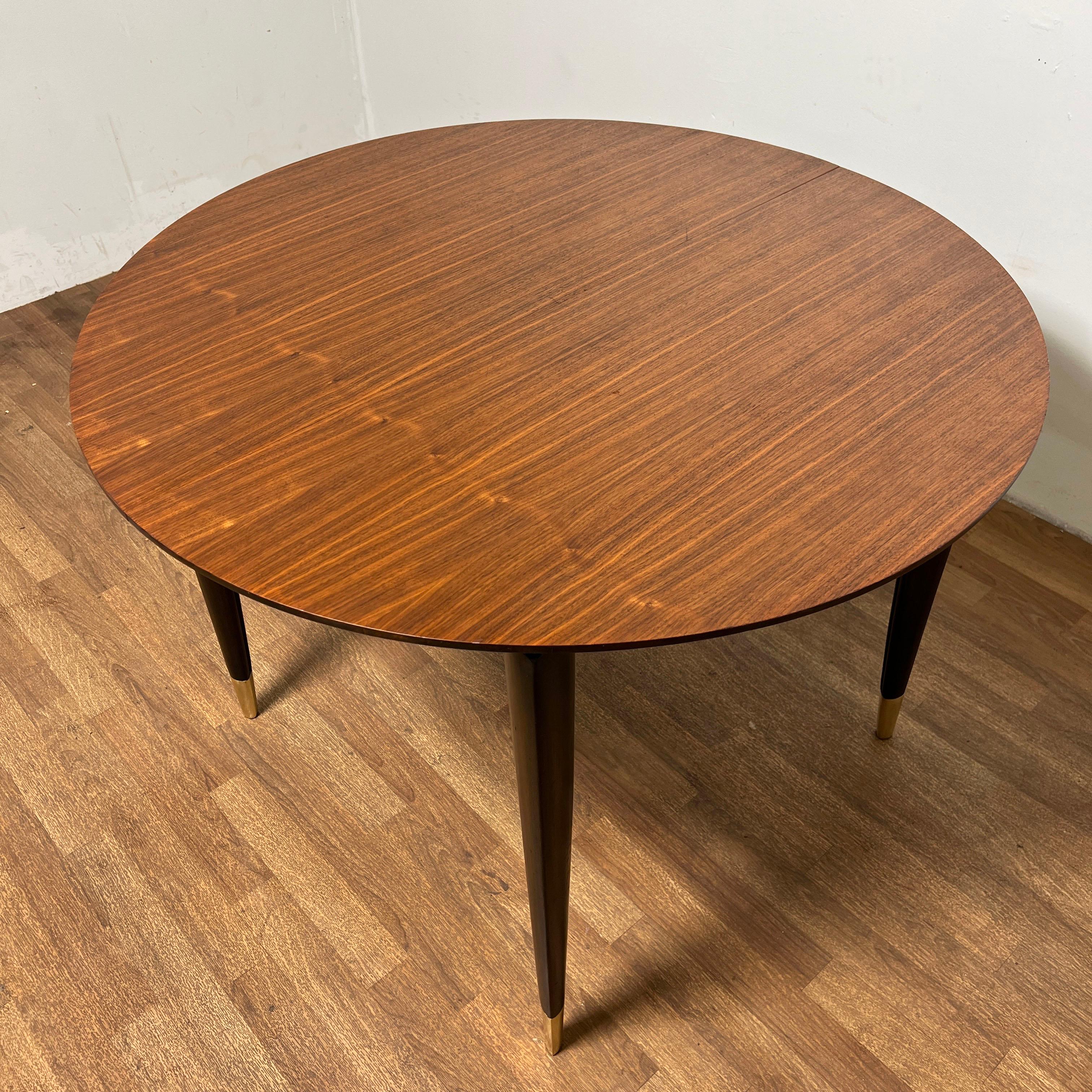 A walnut dining table with brass sabots, designed by Gio Ponti and produced by M. Singer & Sons, ca.  1950s. Measures 40” in diameter, plus one 16” leaf. 
