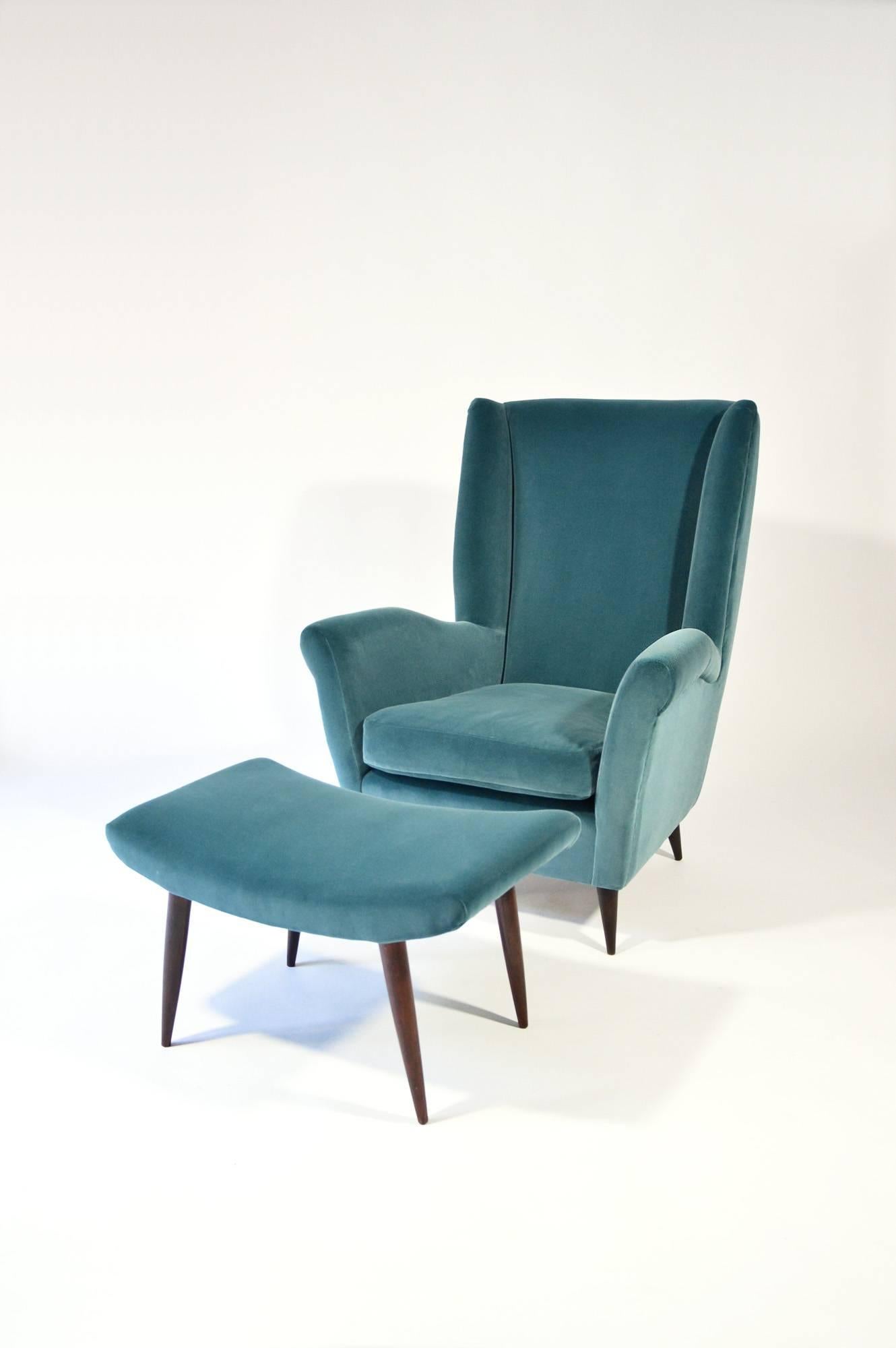 Very comfortable and elegant high-back armchair and footstool with conical wooden legs, designed by Gio Ponti circa 1950, re-uphostered with high quality stone blue cotton velvet. In excellent condition.