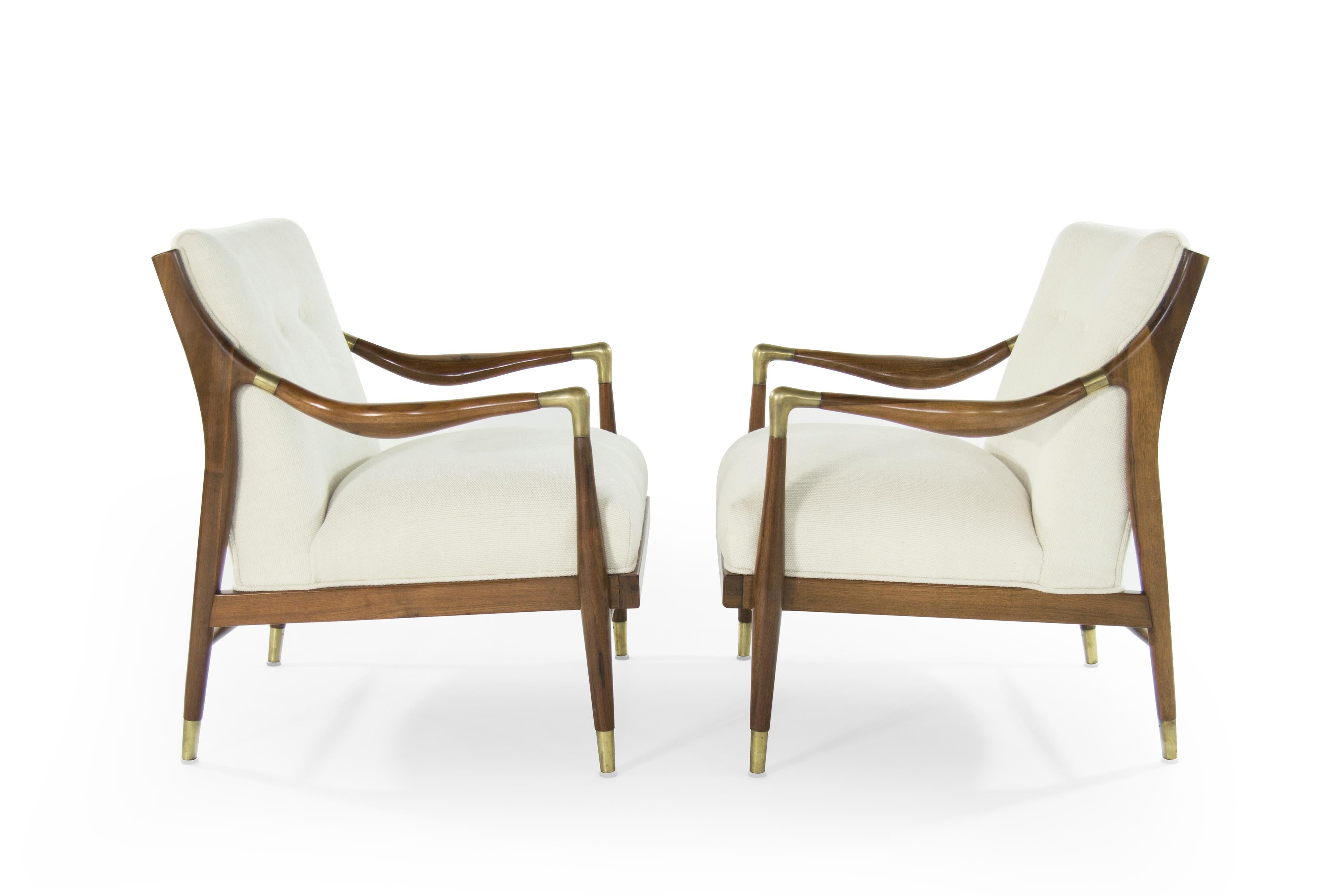 A gorgeous pair of sculptural lounge chairs with brass accents on arms and sabots in the style of Gio Ponti.

Walnut fully restored in a natural finish. Newly upholstered in a off-white twill by Holly Hunt.