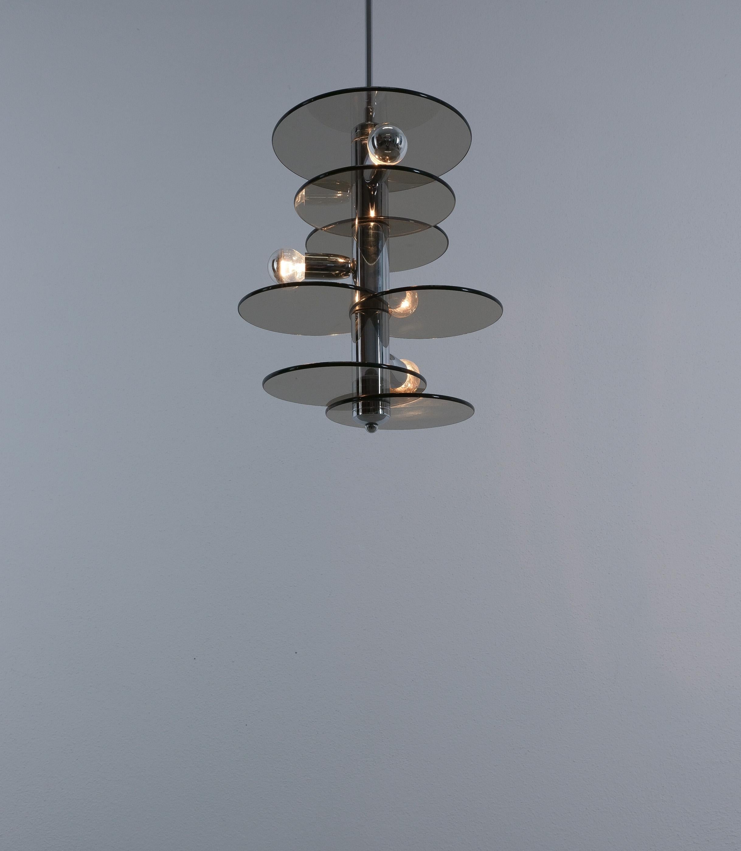 Lampada a sospensione; stile Gio Ponti, 1960 
Bella lampada architettonica con dischi di vetro impilati che orbitano intorno a uno stelo cromato. Realizzato con spessi pezzi di vetro fumé grigio-carbone con bordi lucidi e ottone cromato. In totale