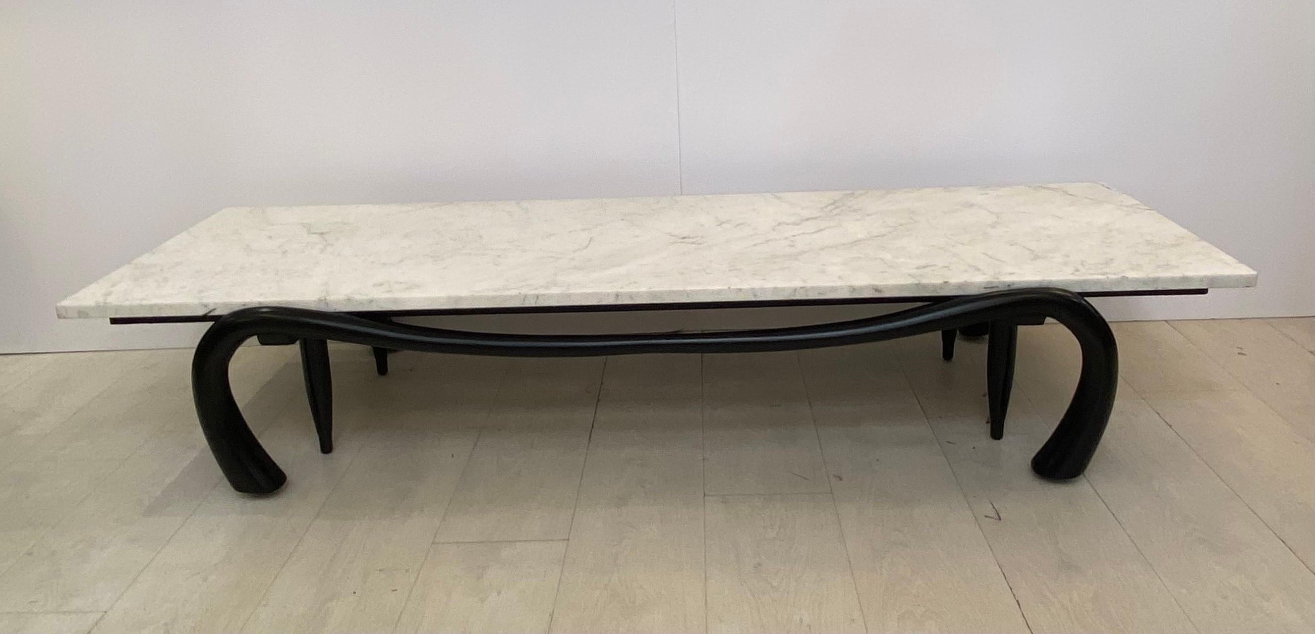 A freeform ebonized wood base with four interior support legs and four carved tapered and bent wooden outer legs… With a carrara marble top… An elegant design with complex construction circa 1960s… 24 inches deep by 68 1/2 inches long by 12 1/2