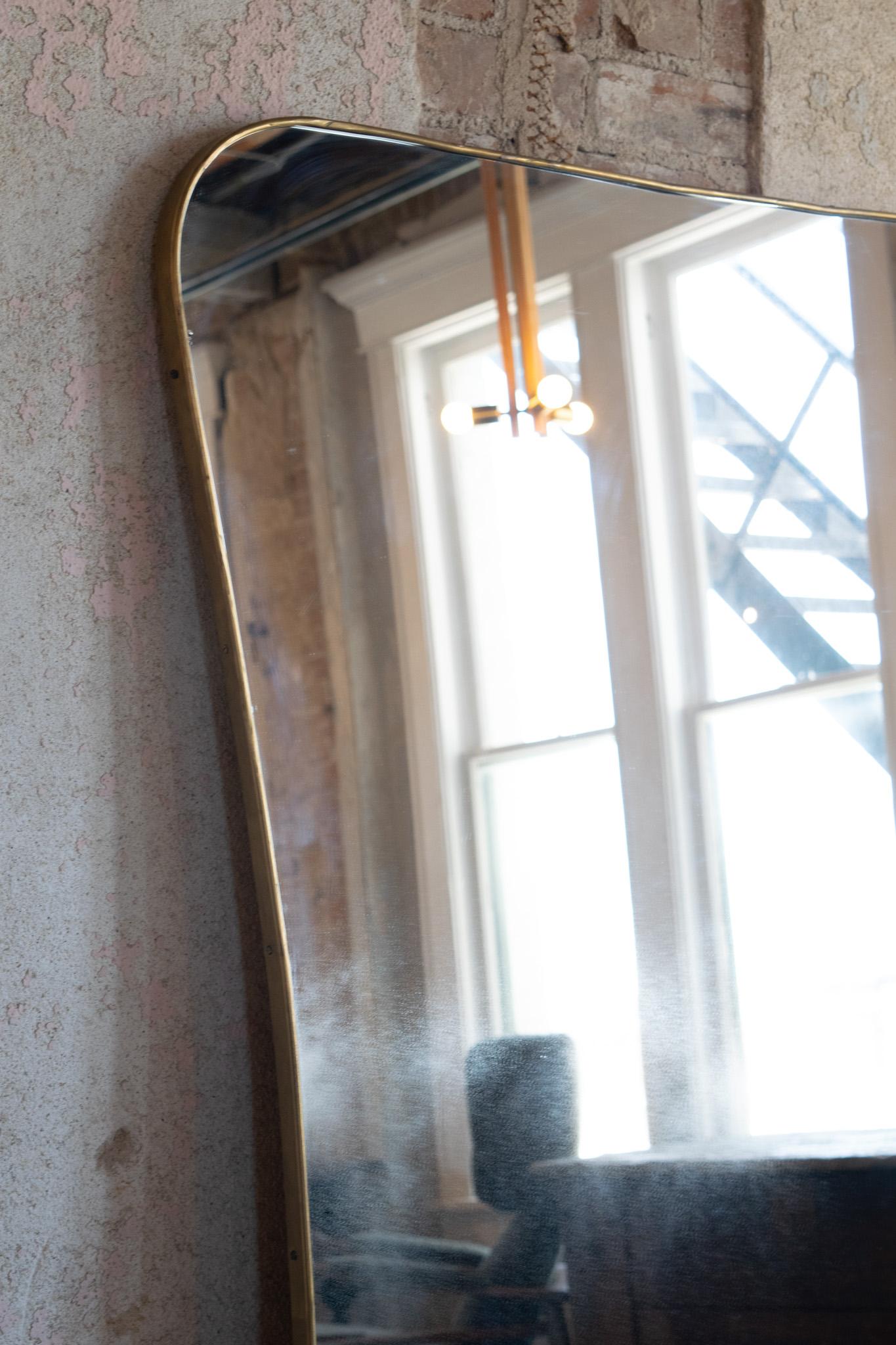 A large scale vintage hour glass shape brass frame mirror in the style of Gio Ponti. The piece is in overall good condition with some age on the mirror and minor separation between the glass and frame in two areas. The width ranges from 37-42