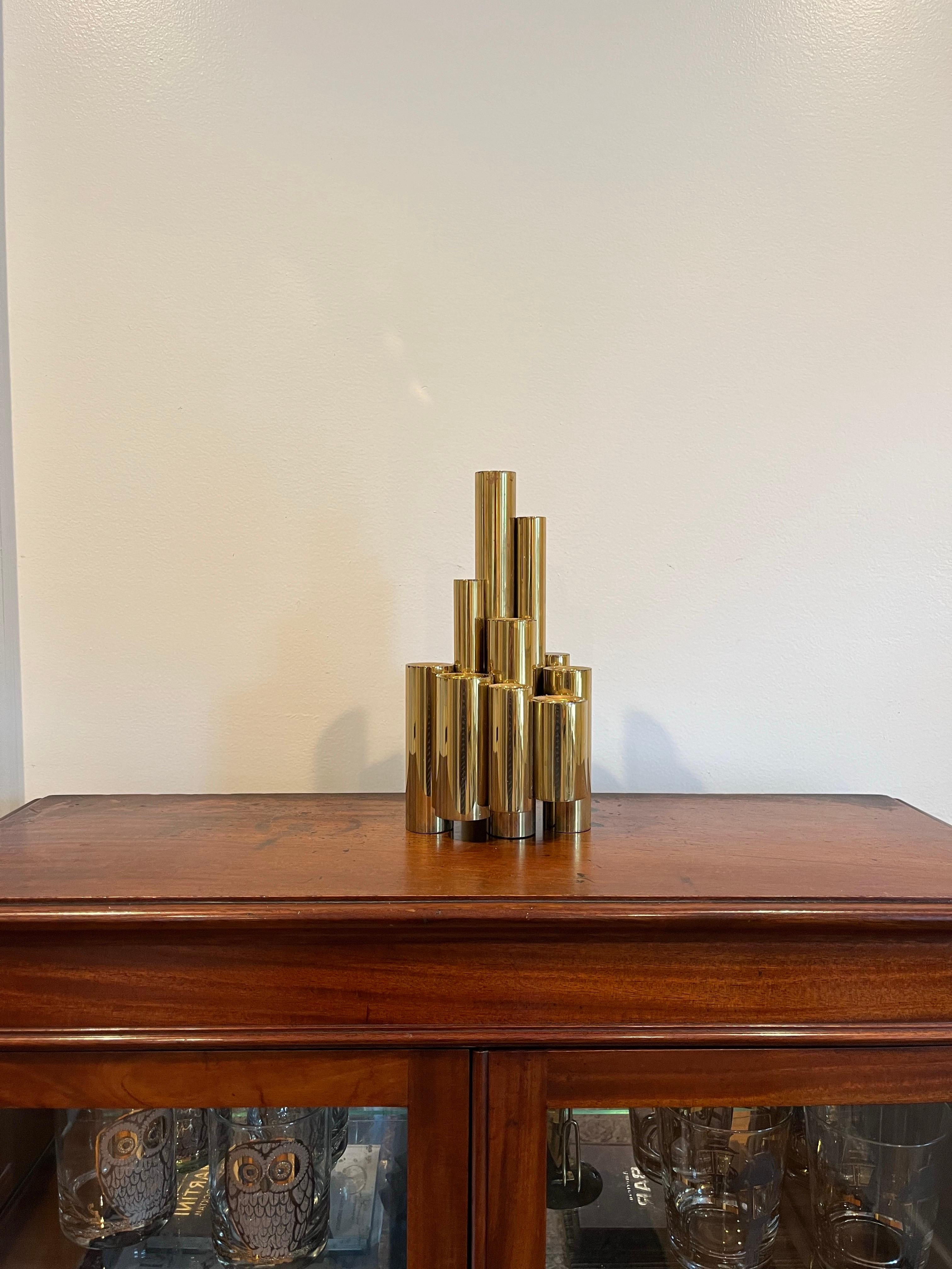 Polished brass candlestick composed of alternating heights of tubular elements.