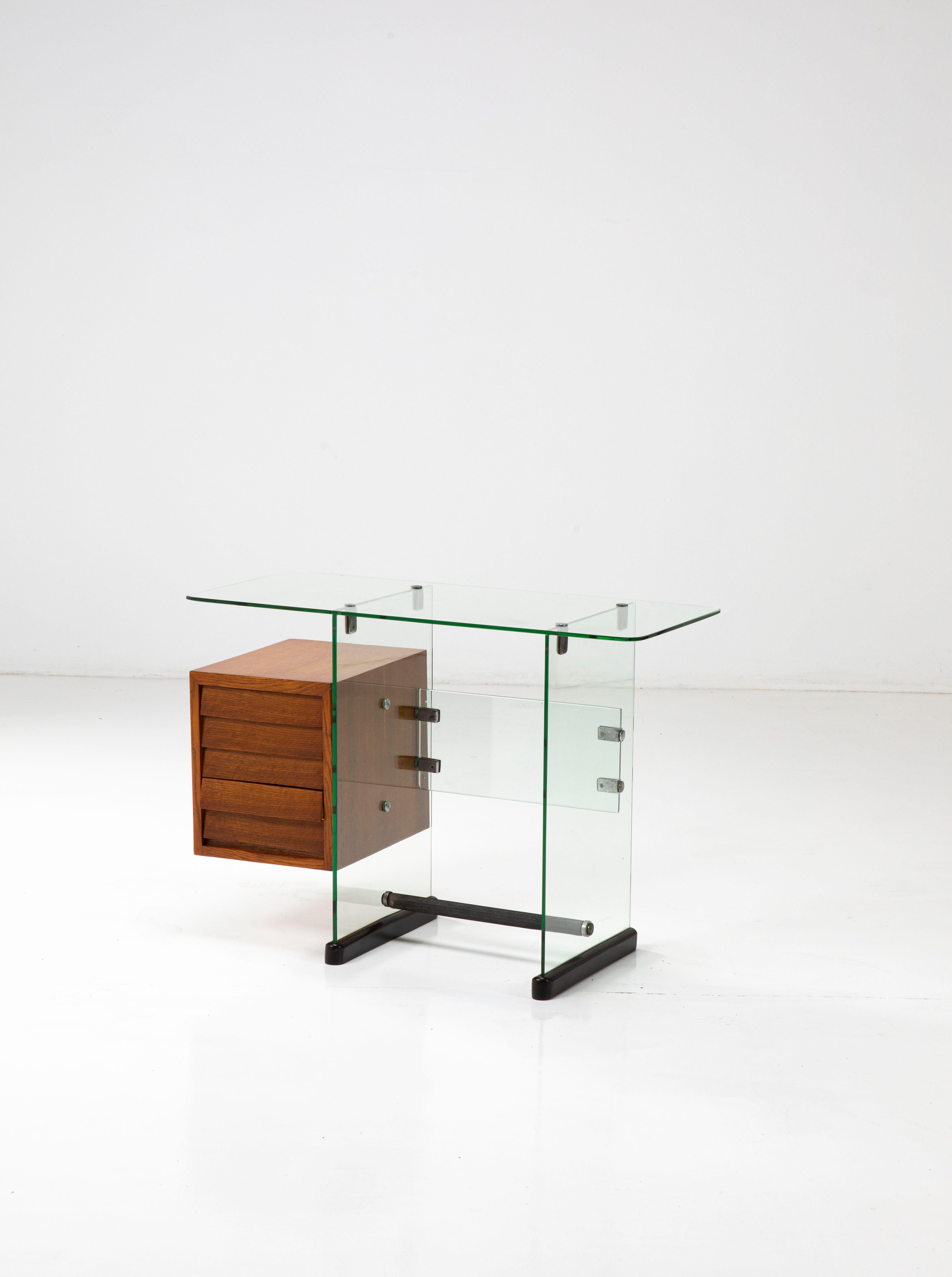 This elegant small desk is made of toughened glass panes joined by brass and metal junctions and with a wood chest of drawers, just as the two bases are made of wood. 

The design of this piece is related to other office furniture created for