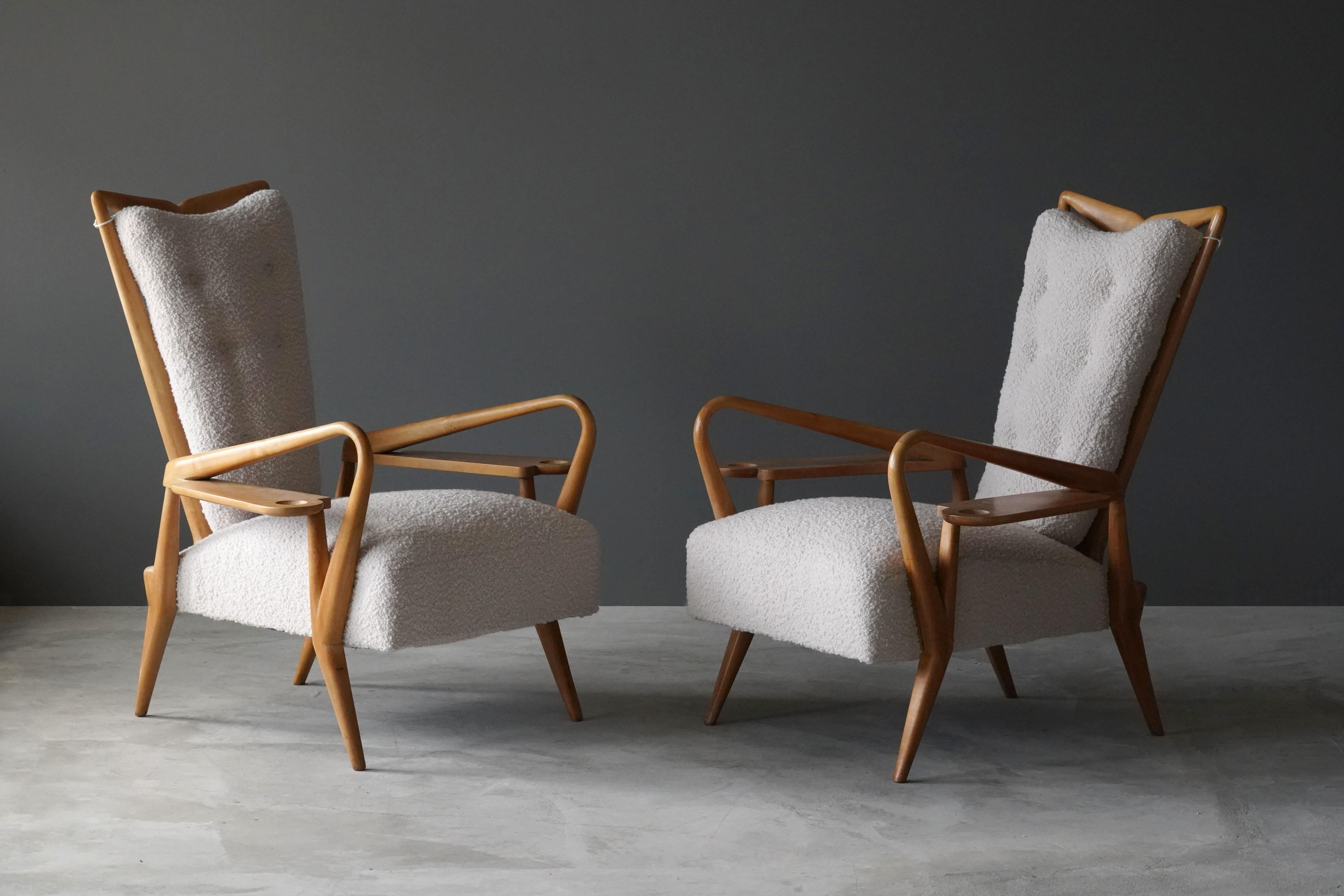 A pair of highly modernist and organic lounge chairs / highback chairs in finely carved maple, reupholstered in off white bouclé. Design attributed to Giordano Forti. Produced in Italy in the 1940s. The design incorporates side tables built onto the
