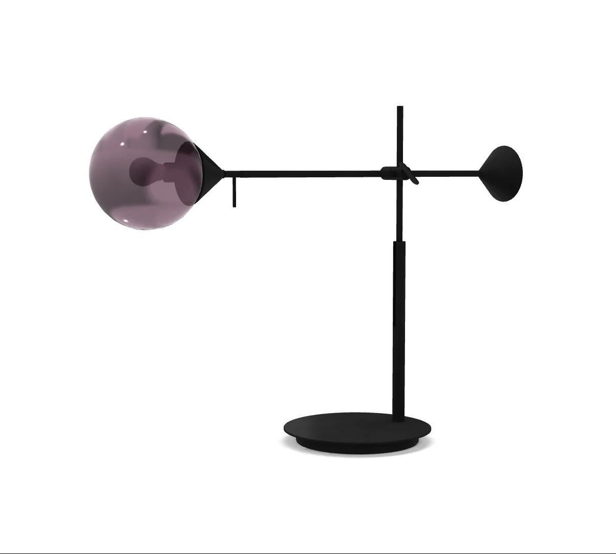 The Kendama Table Lamp features a burnished metal and light structure paired with hand-blown Murano glass spheres. It features a sleek black frame complemented by amethyst-colored glass, highlighting a blend of refined craftsmanship and contemporary