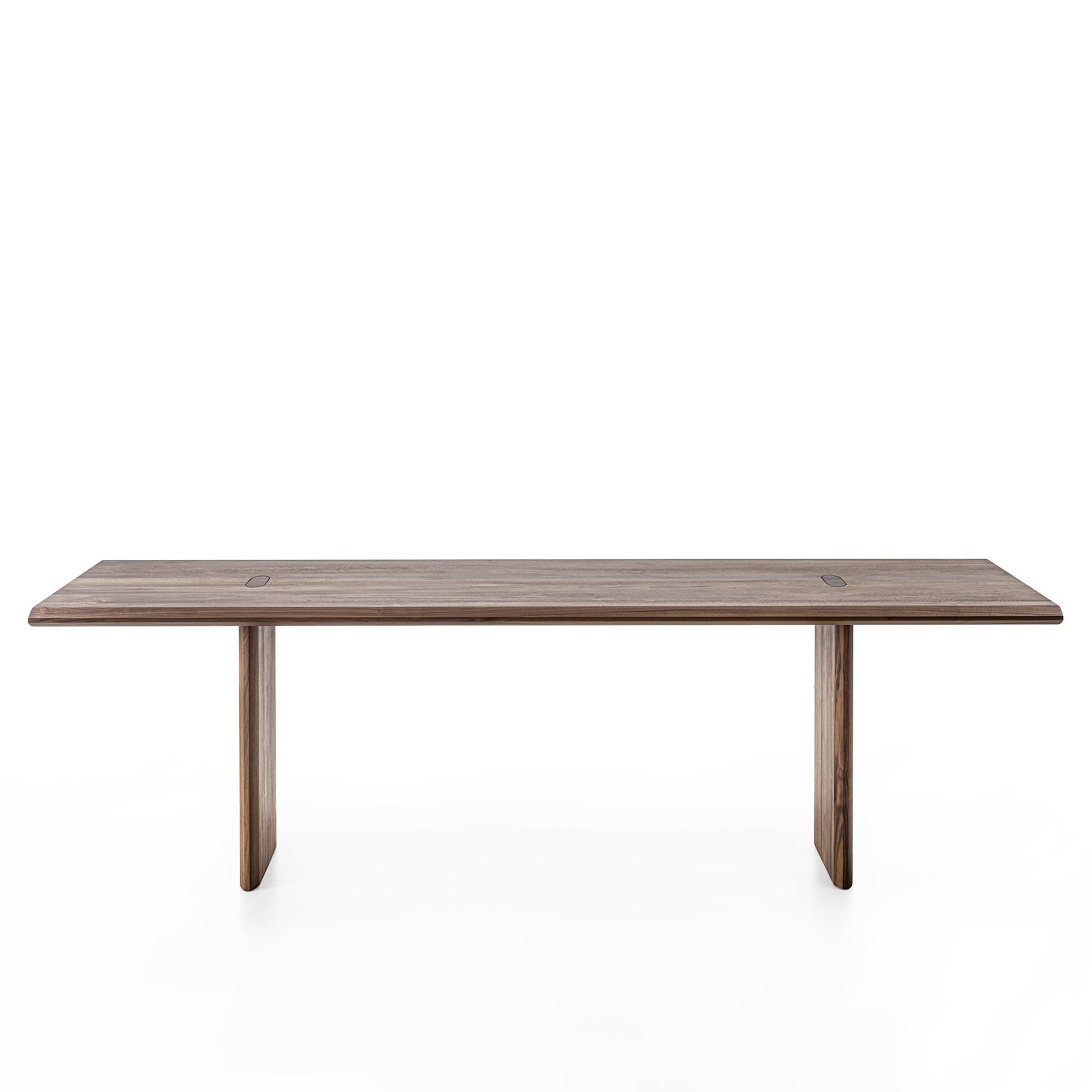 Table de salle à manger Giorgia en noyer avec structure en bois massif
bois de noyer en finition naturelle, plateau de table avec chants collés 
douves avec pattes traversantes visibles et articulation caractéristique. 
La géométrie de