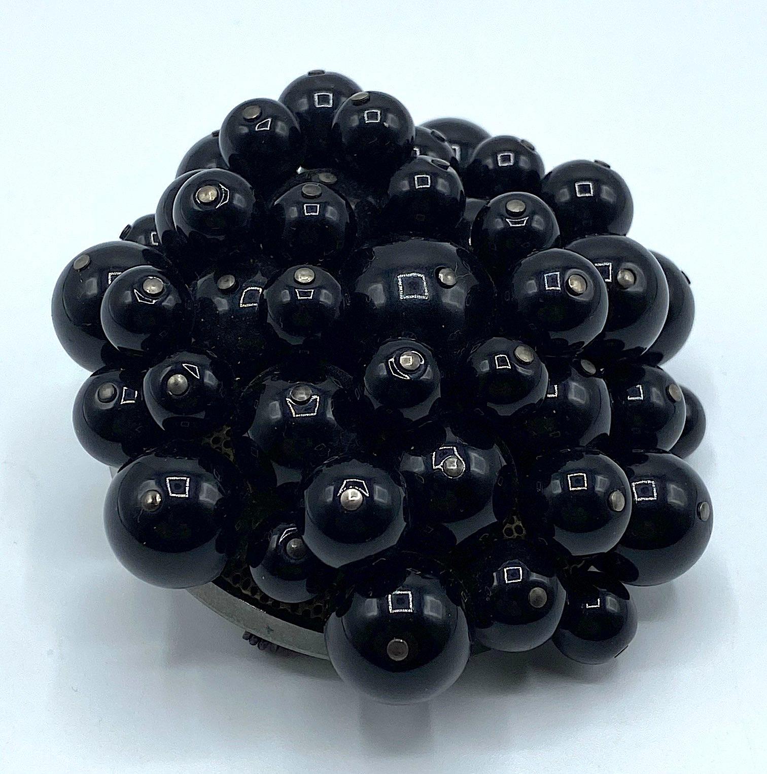 A true statement piece and unique design is this brooch. It is comprised of four sizes of black resin beads individually threaded onto a pin and attached to a lightly domed round mesh top piece. The mesh dome is, in turn, set into a solid charcoal
