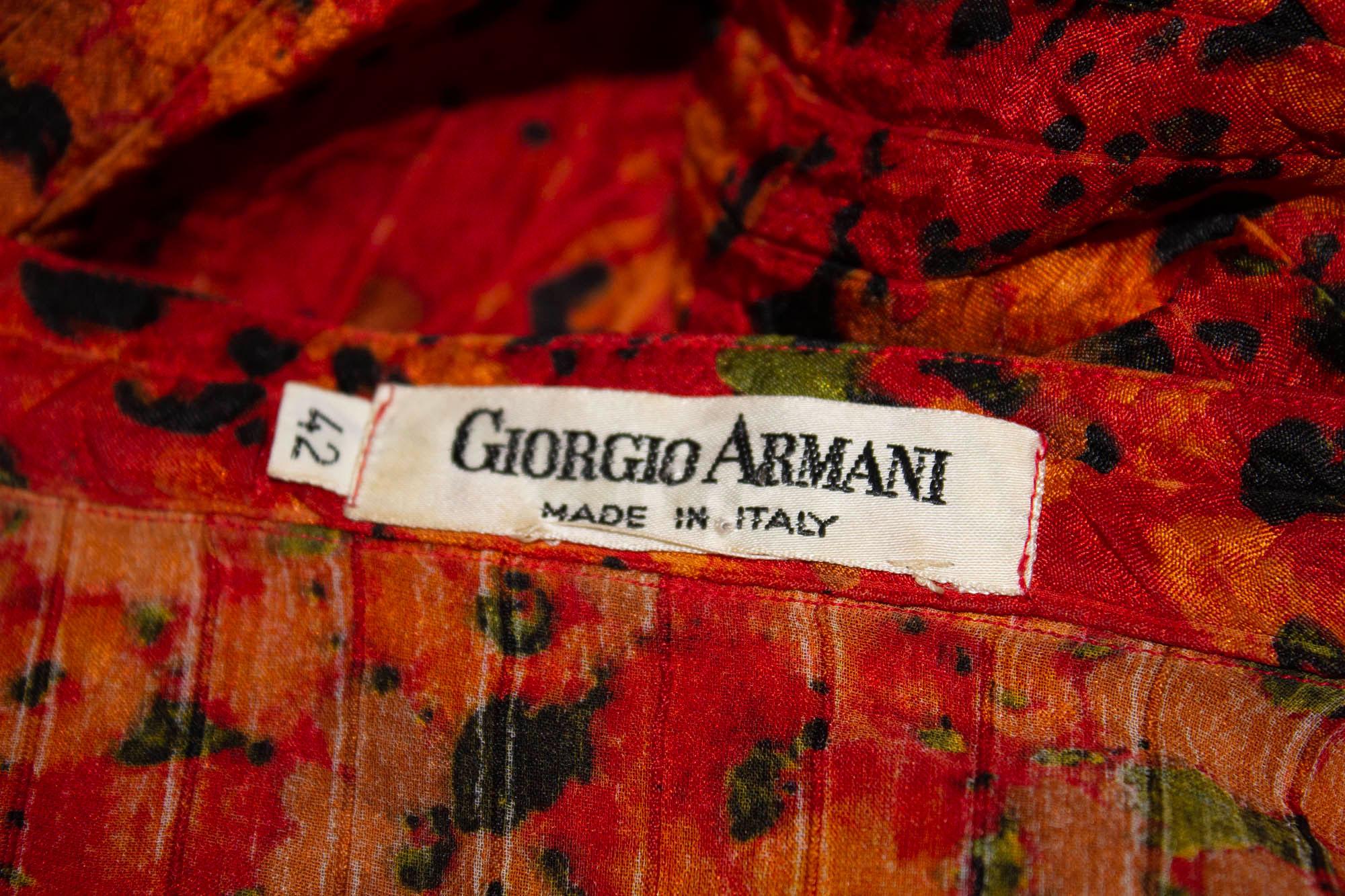 Eine schöne Vintage-Seidenbluse von Giorgio Armani. Die Bluse aus farbenfroher, strukturierter Seide, einem Mix aus Rot, Orange und Schwarz, hat einen Stehkragen, eine Knopföffnung vorne und Manschetten mit einem Knopf. Eu Italienisch 42 , Maße: