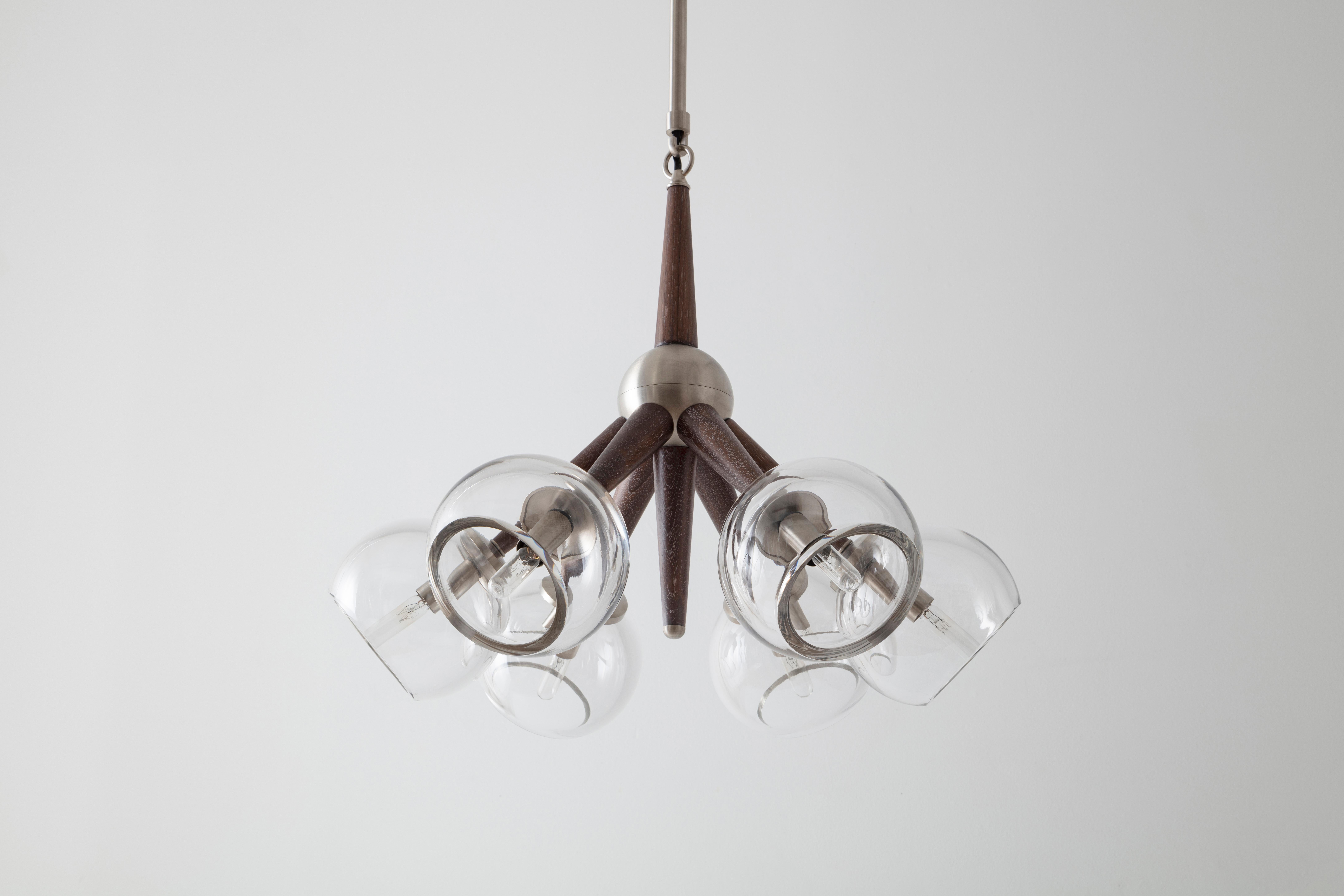 Giotto Burst is a modular chandelier inspired by 20th century space exploration. Tapered wooden arms cradle an array of hand blown globes available in clear or smoke glass. Material finishes, arm length, and positioning can be customized to create