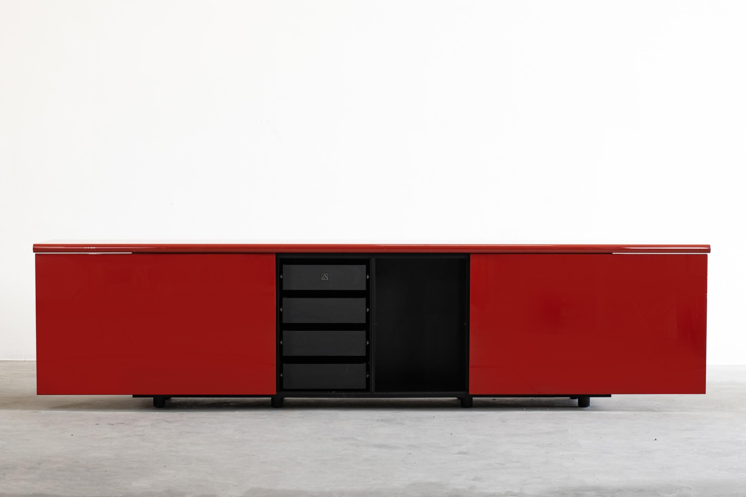 Giotto Stoppino Sheraton sideboard with a storage compartment consists of two sliding doors that slide outward to expose sections for shelves and four drawers on the left-hand side.
External structure in red lacquered wood, laminated interior, and