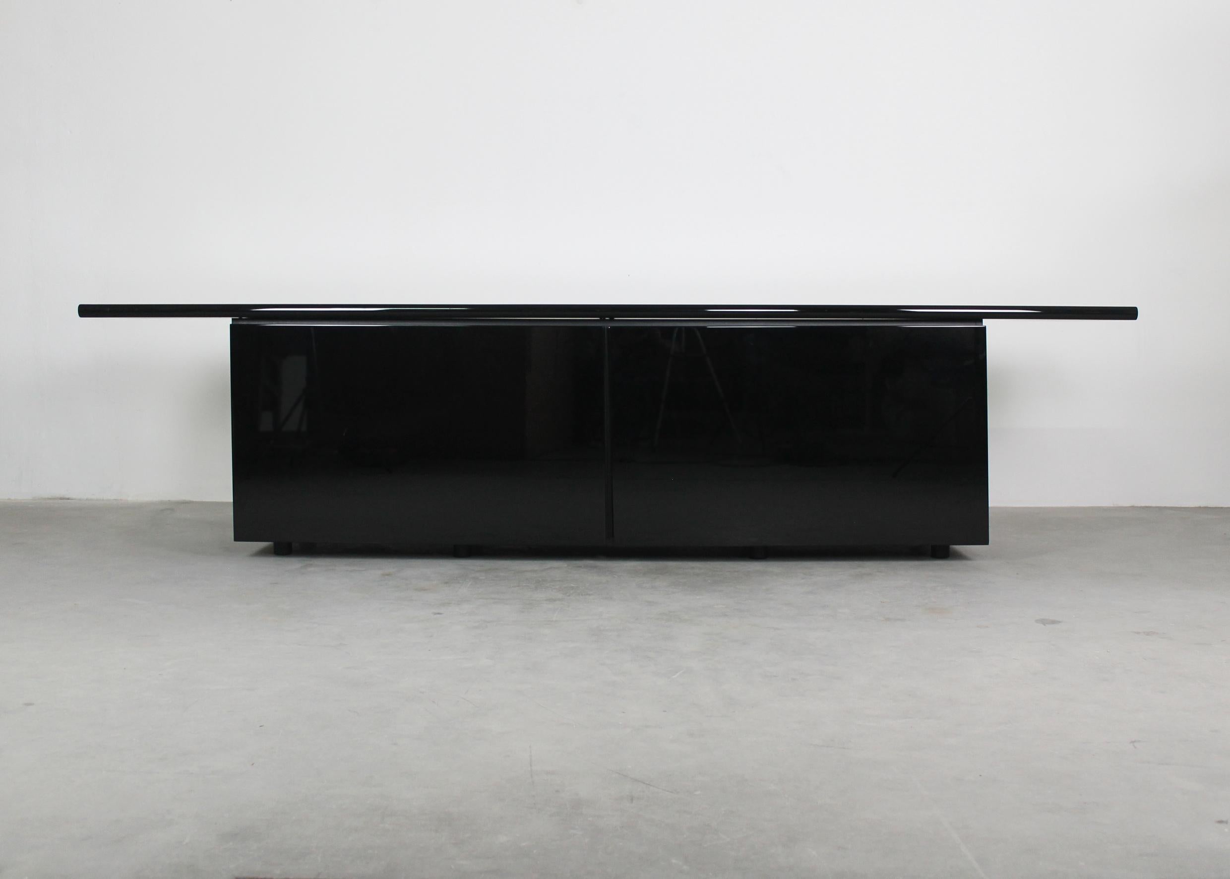 Sheraton sideboard presents two sliding doors that slide outward to expose three inner storage units with glass shelves and four drawers on the central part.
The sideboard has a structure is in black (with a glossy finish) lacquered wood,