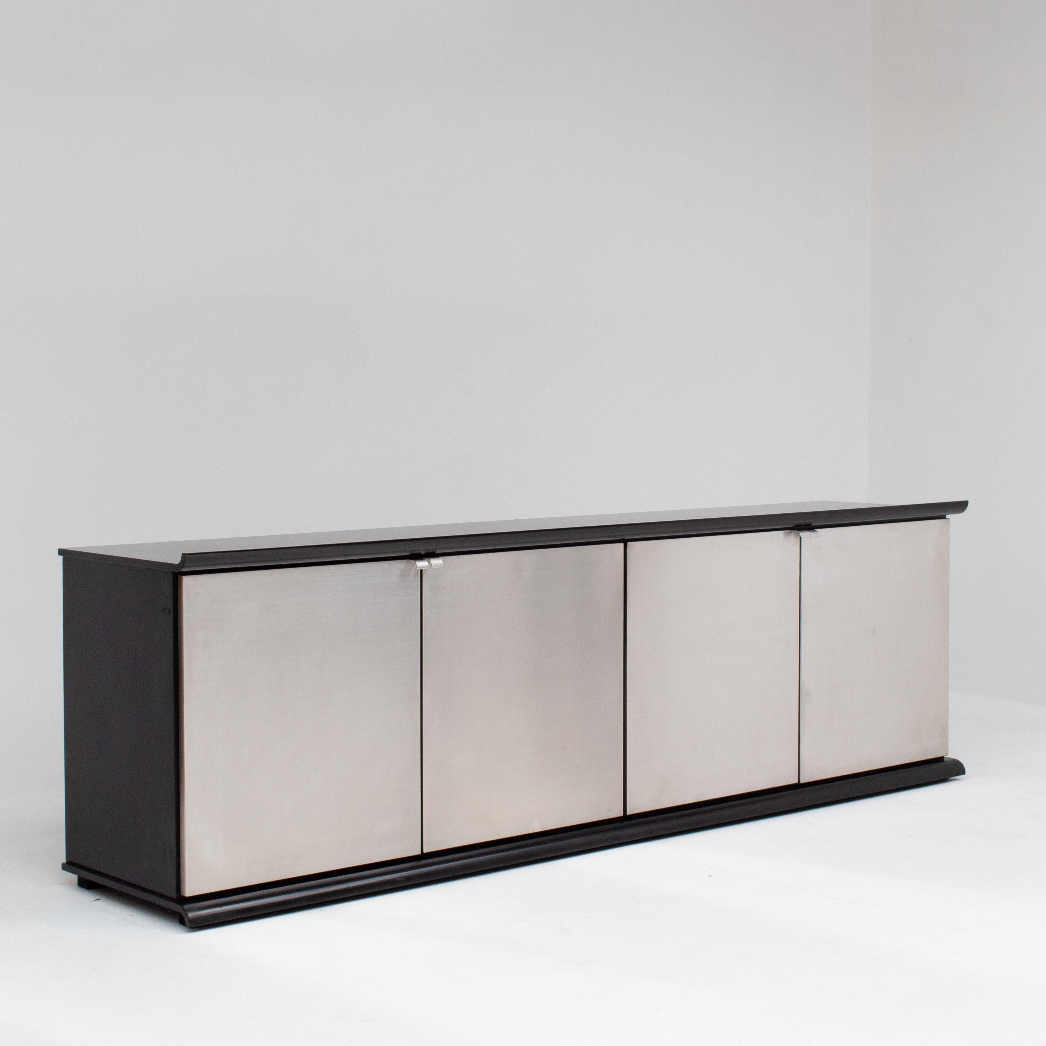 Questa rara credenza di Giotto Stoppino per Acerbis è un raffinato esempio di modernismo italiano degli anni Settanta. Il design minimalista combina una struttura in legno laccato nero profondo con quattro ante in acciaio spazzolato, creando un