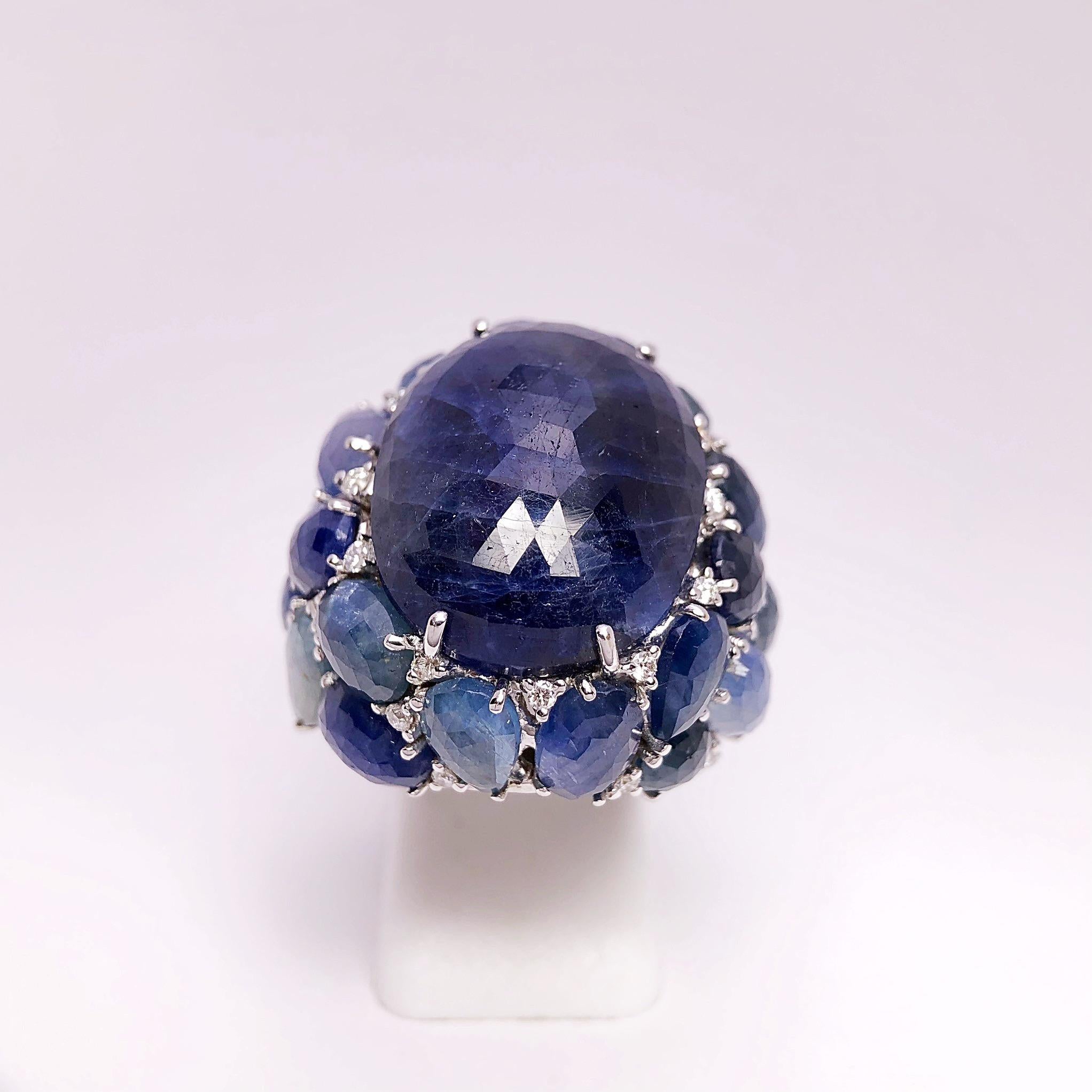 Creado por Giovanni Ferraris de Italia , este anillo de zafiro es una obra de arte. El zafiro opaco ovalado azul oscuro central es un cabachón facetado briolette que mide 22 mm x 16,5 mm. . El anillo tiene un engaste espectacular diseñado con azul