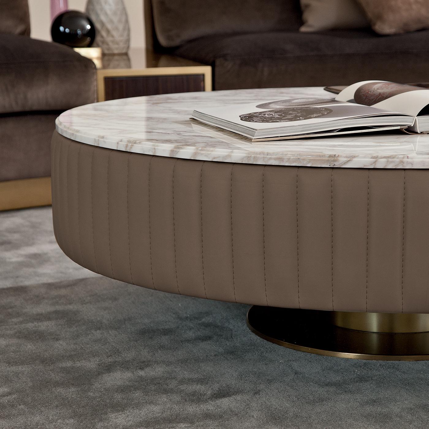 This majestic circular coffee table has a solid linden wood structure that takes center stage with its eye-catching details. Its large Calacatta gold marble top is framed with a large rim upholstered in grosgrain gray leather (in the picture: