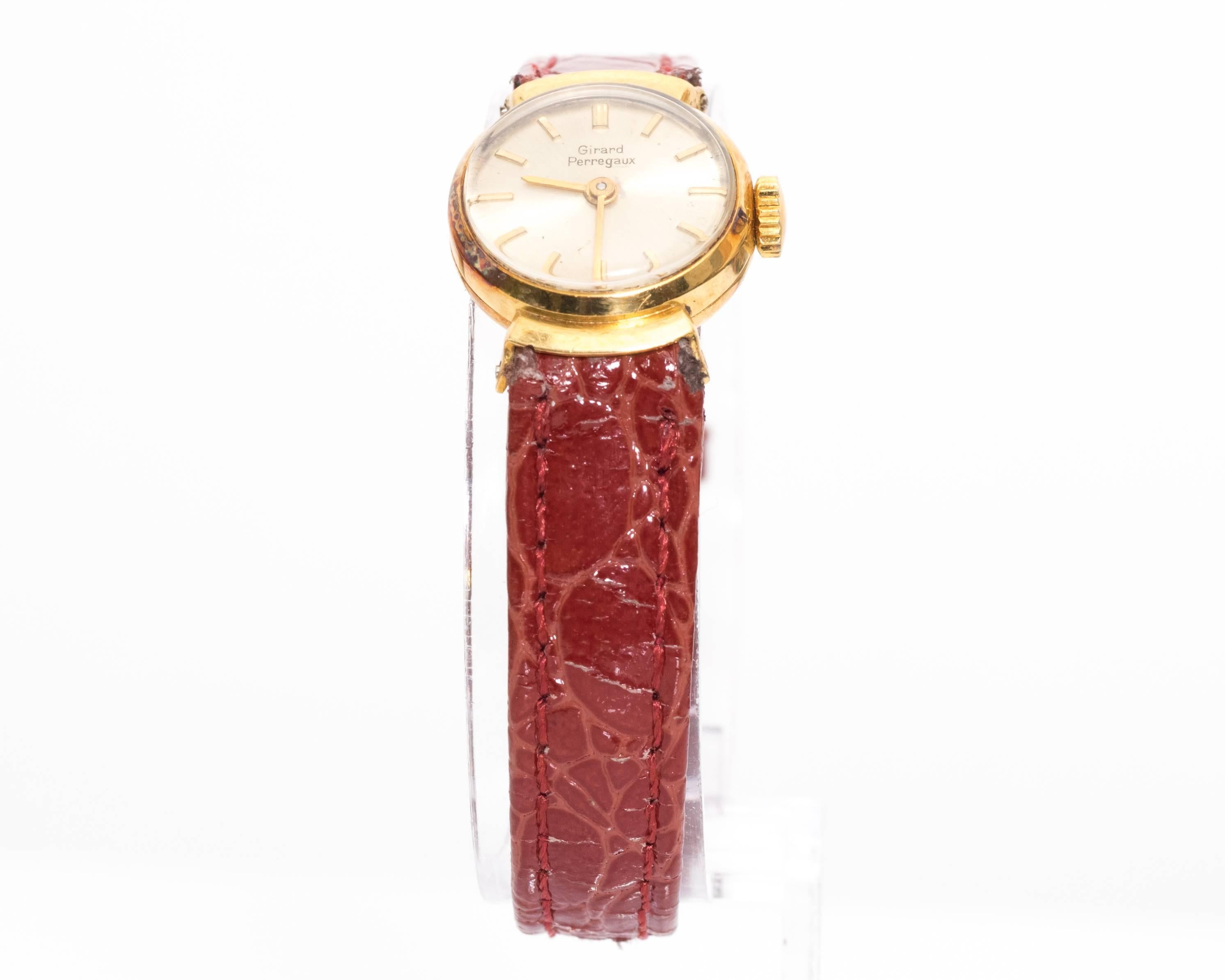 1950s Girard Perregaux Ladies Wristwatch
Yellow Gold
Made in Switzerland
Winding movement watch
Patina on Metal, common due to age of watch. Hints of rainbow color on case. 
Fits 7.5 inch wrist
Case Size is 16 millimeter

Band is an after market red