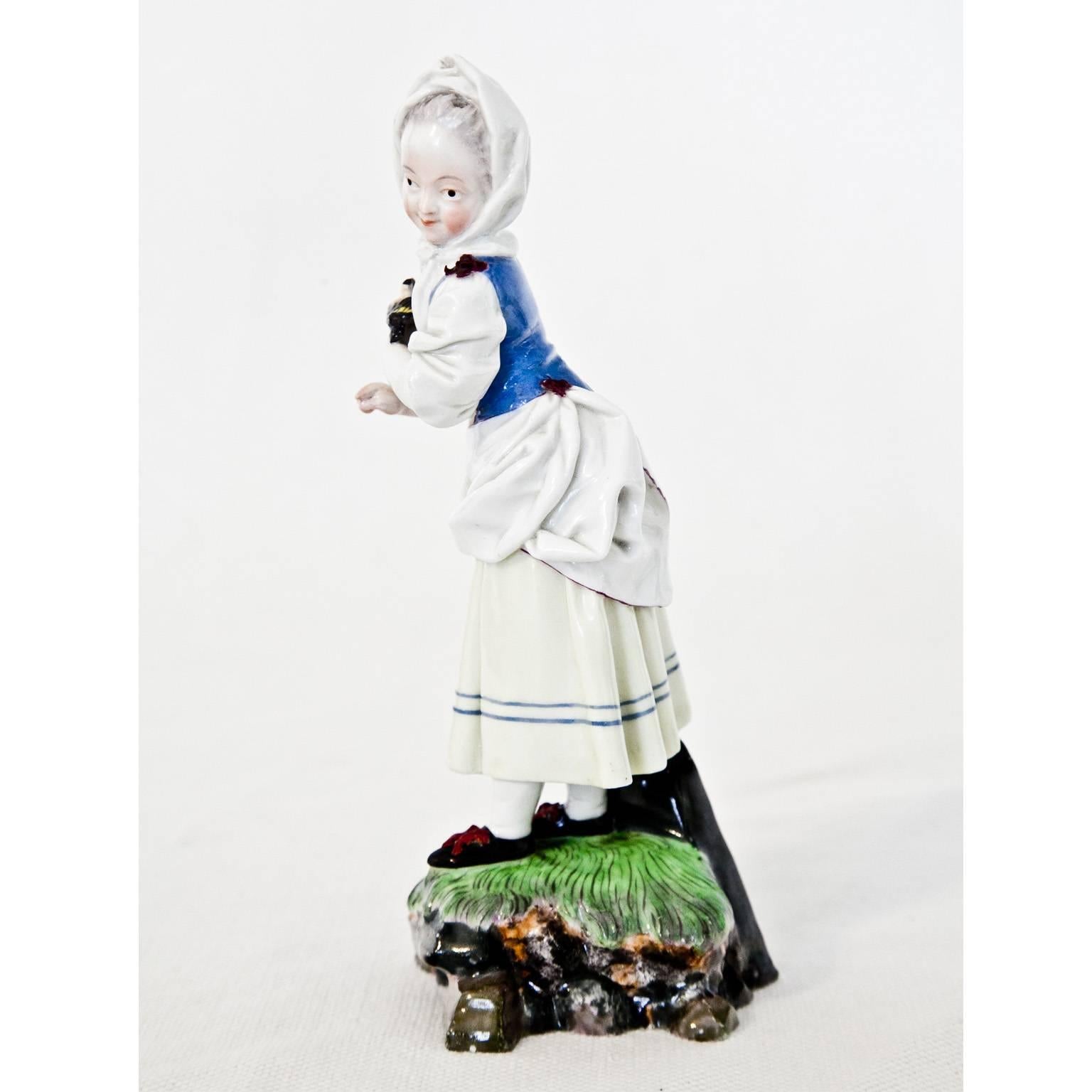 Polychrome porcelain figurine of a girl with a white bonnet and a little bird in her hand, standing on a landscape base. Design by Johann Peter Melchior, blue mark at the bottom of the porcelain manufactory Höchst.