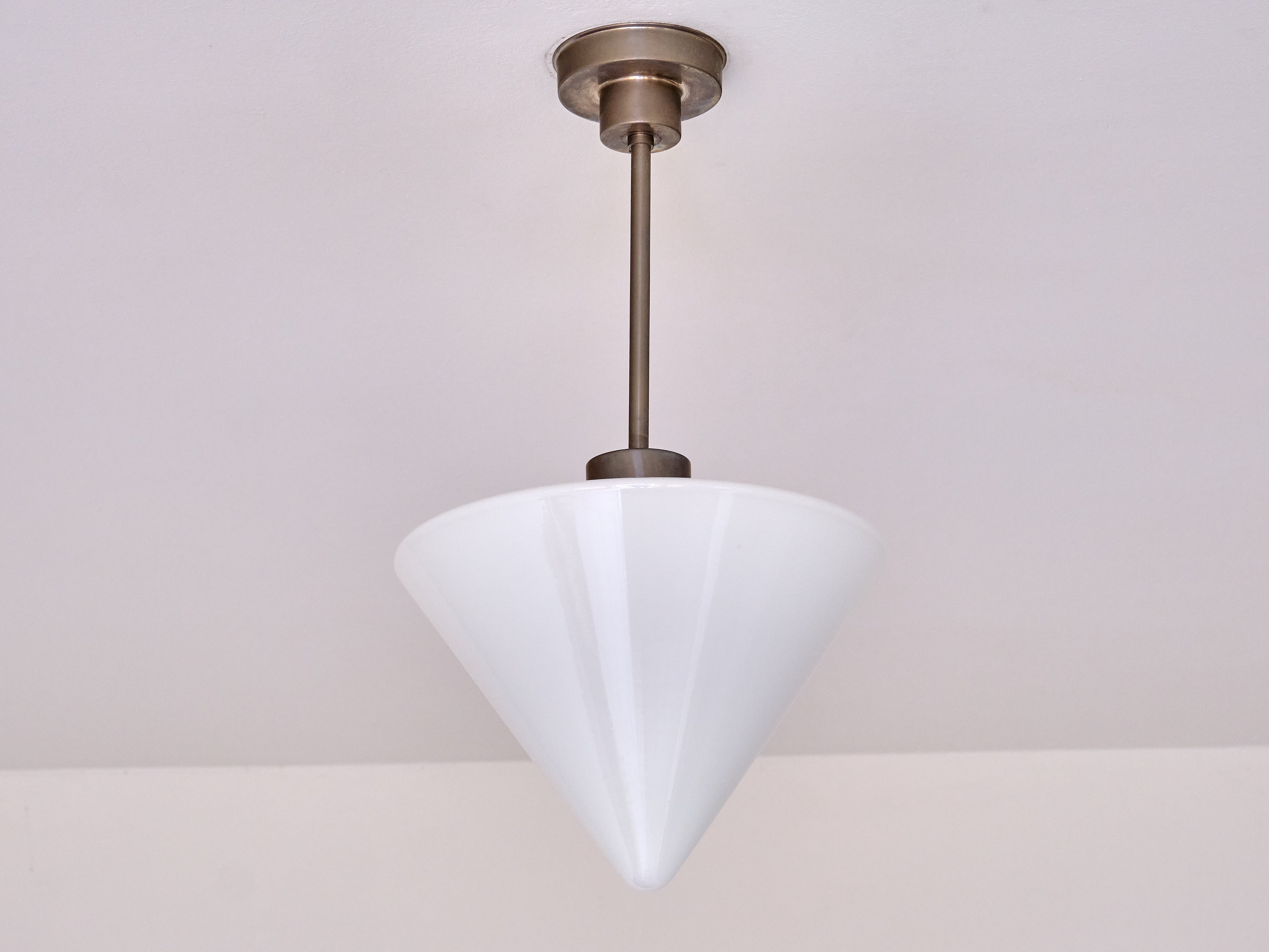This rare pendant light was produced by Gispen in The Netherlands in the 1950s. The striking cone shaped shade is made of a slightly glossy, white opaline glass. The shade is attached to the two-tier fixture made in a matte nickel, with a beautiful
