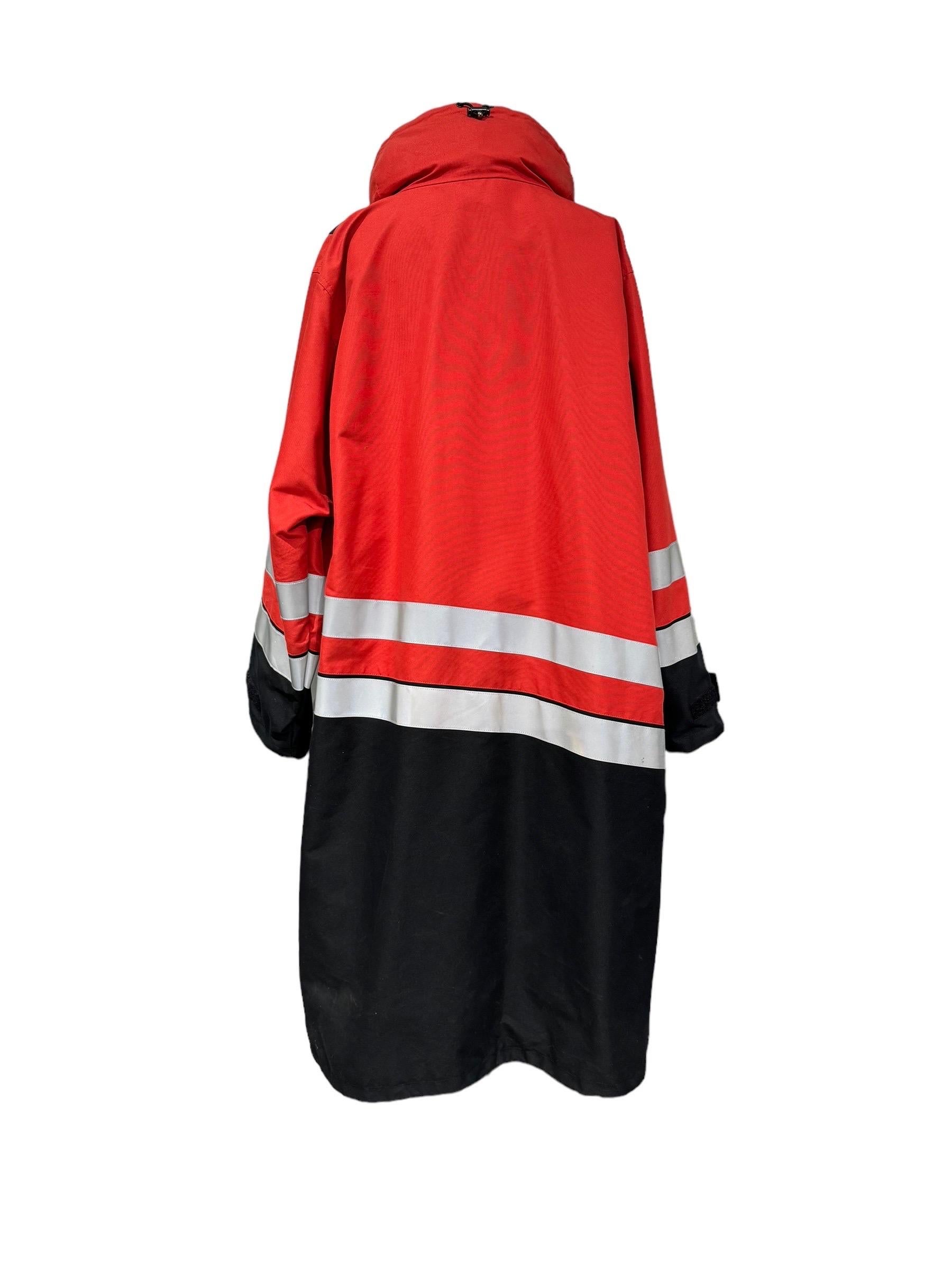 Giubbino firmato Balenciaga, realizzato in tessuto impermeabile di colore rosso e nero. Presenta sulla parte frontale una targhetta con logo, una zip in plastica nera e una chiusura a strappo. Munito di due tasche laterali, una con zip, l'altra con