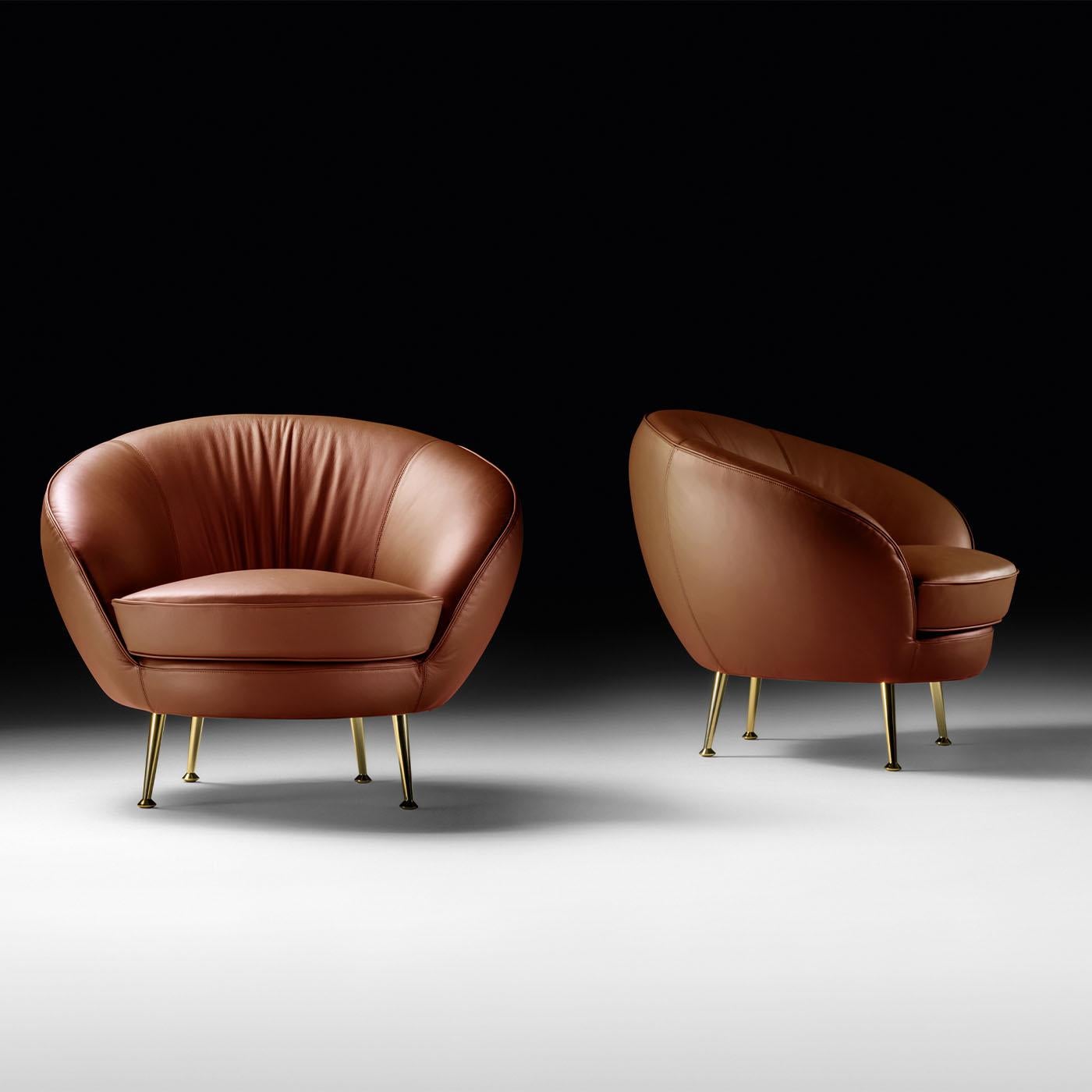 Stiletto feet in a refined metallic finish sustain the welcoming seat distinguishing this armchair. Prized brown leather fully envelops the seating unit, where the plush seat cushion is embraced by a flared-cut shell whose sides harmoniously slope