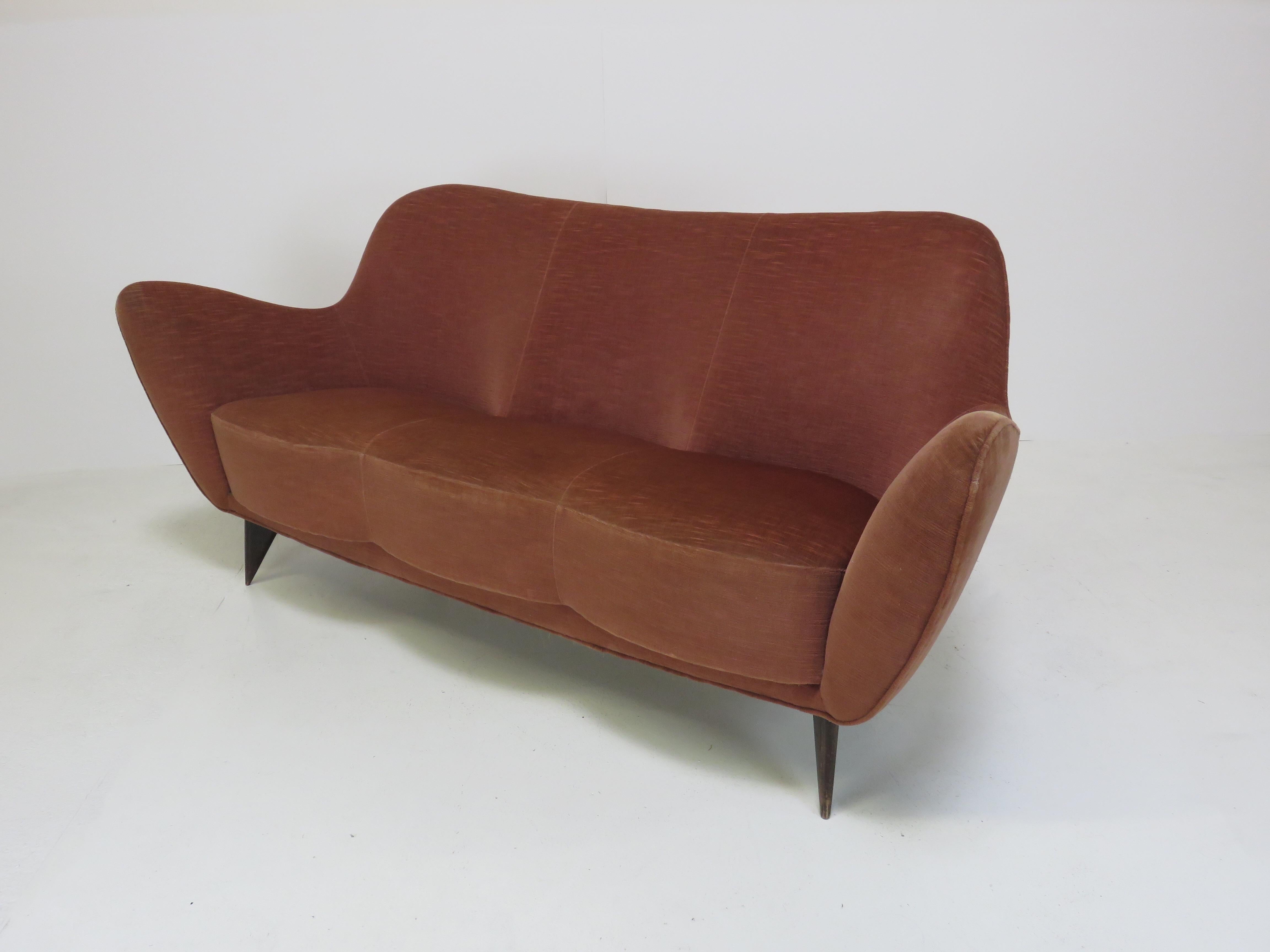 A sofa with three individual seats and a curved back on each section. Tapered wood legs. 
Made for ISA Italy, c. 1952.
