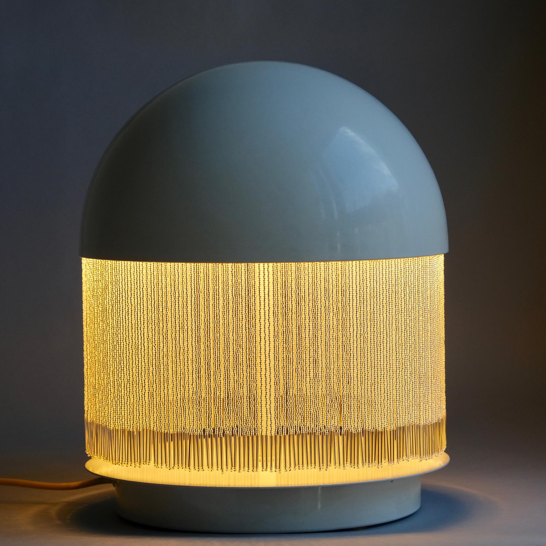 The half-spherical white lacquered shade issuing a transparent-beaded fringe, on a cylindrical central stem, on a flat round terrace.
Produced by Quattrifolio, Milano,
circa 1979.

Literature
G. Gramigna, Repertorio del design italiano