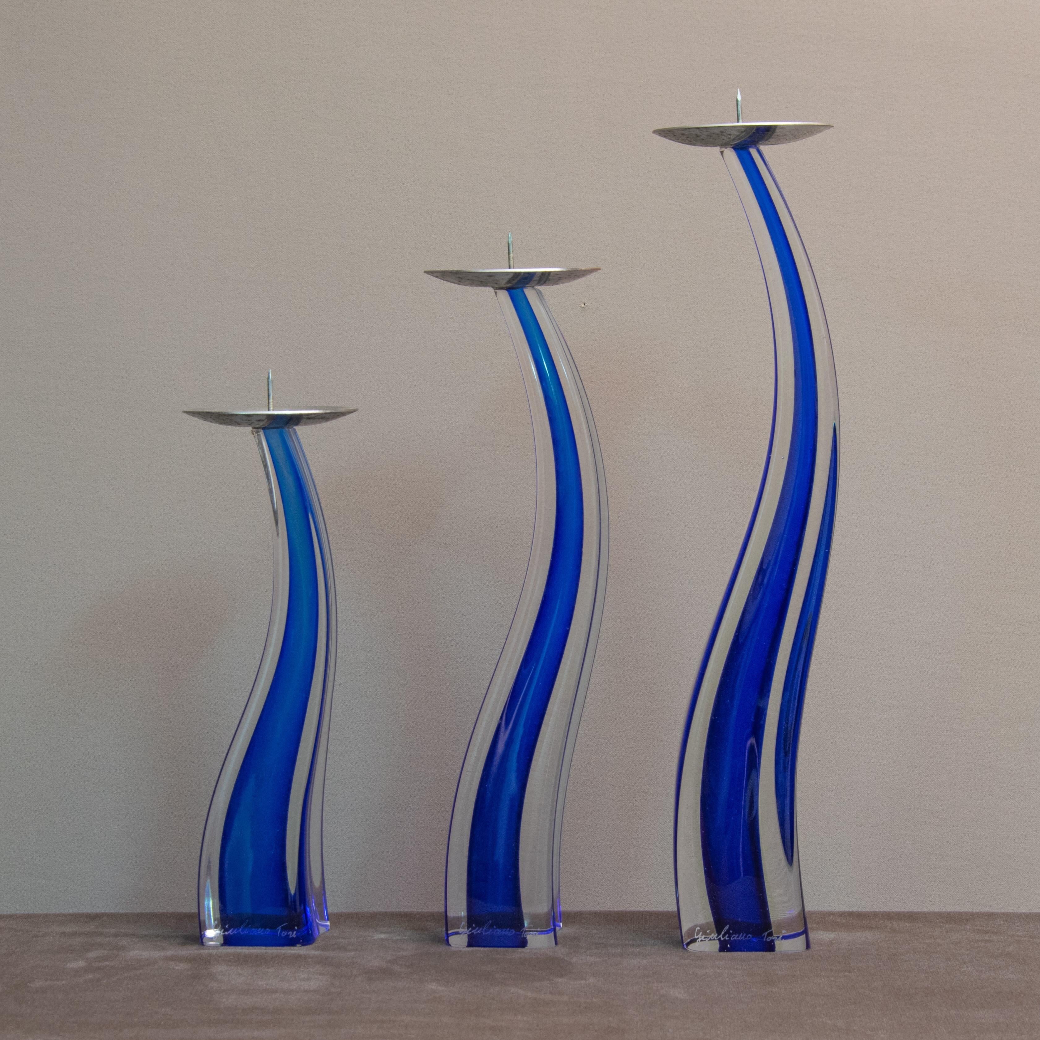 A set of three hand blown curves Cobalt Blue glass cased in clear glass. Murano glass candlesticks designed by Giuliano Tosi for Oggetti in the 1980s.
All three candle sticks are signed by Giuliano Tosi
Measurements:

Measures: Large 12.75 high x