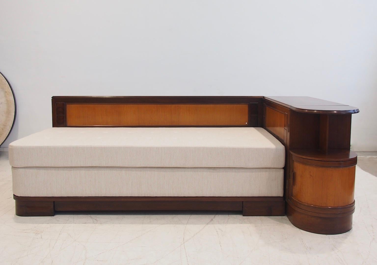 Lit de jour angulaire Giuseppe Gibelli plaqué en noyer et acajou. L'appui-tête contient une table de chevet avec des étagères et des tiroirs. Nouveau matelas et revêtement en tissu.
