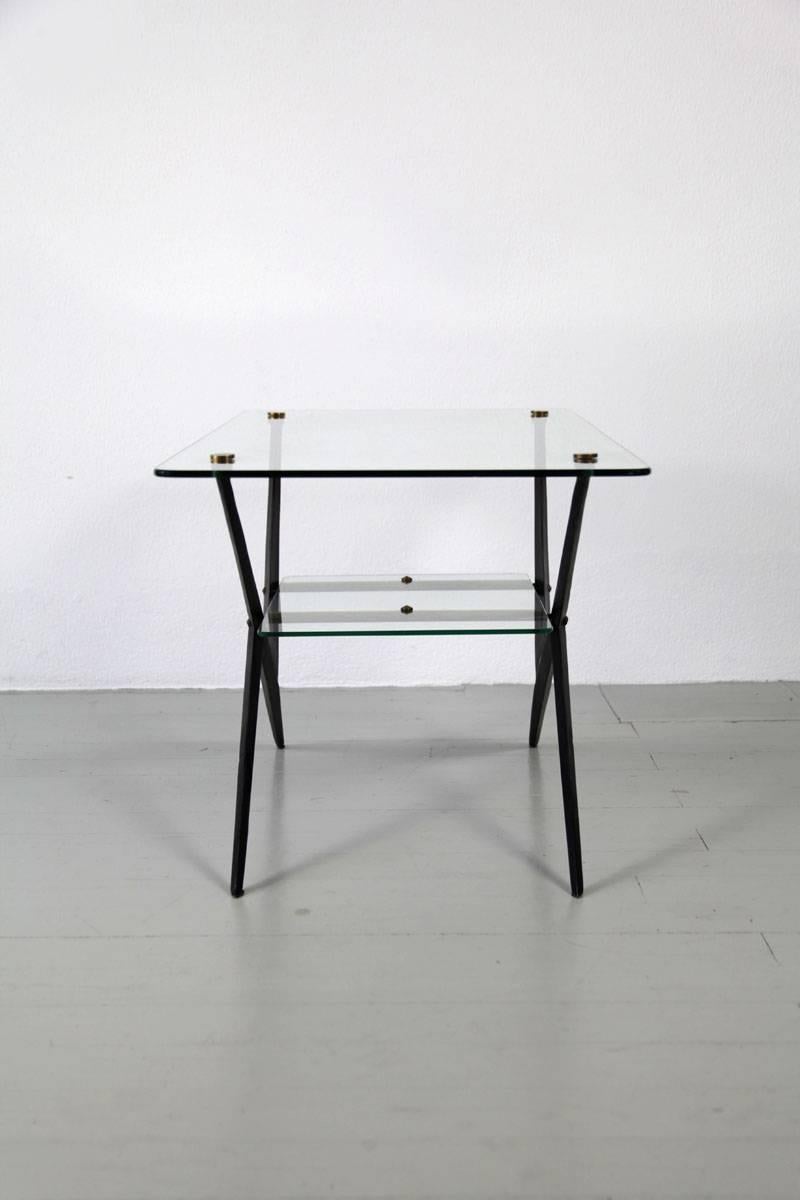 This Italian side table was designed by Giuseppe Ostuni and manufactured in the 1950s. The extravagant table has two levels with glass tops that rest on the black lacquered iron frame with brass elements. The angular shapes and unusual composition