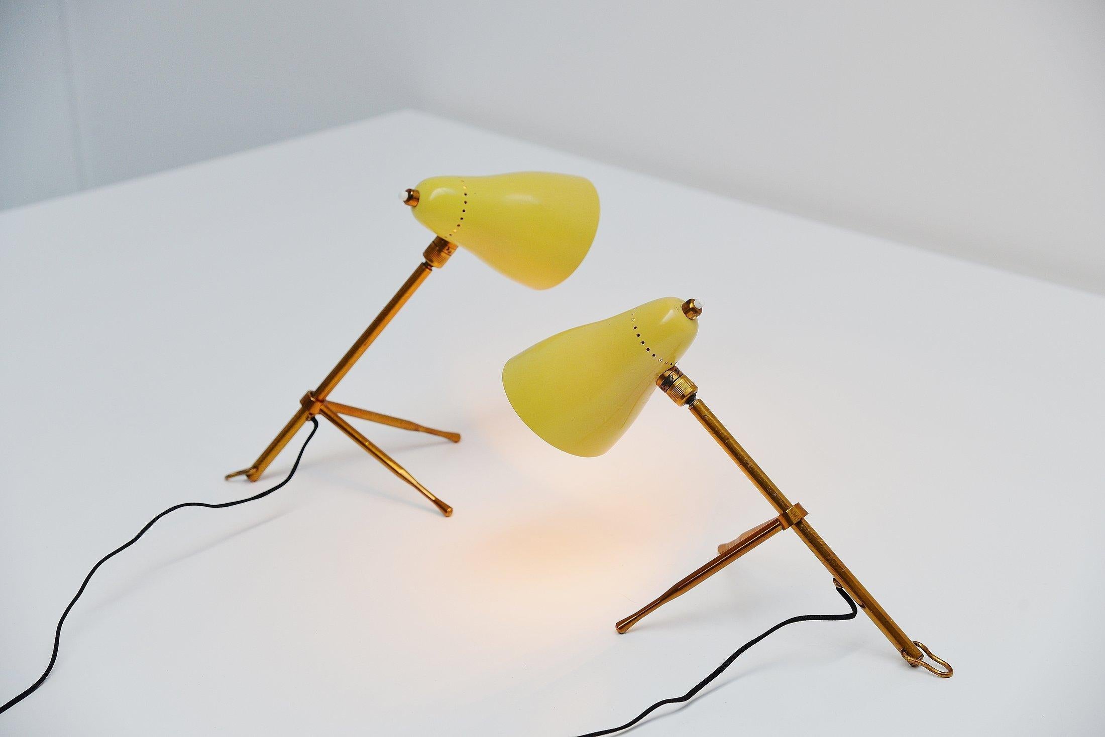 Very nice pair of table lamps model 215 designed by Giuseppe Ostuni and manufactured by Oluce, Italy 1949. These lamps are from the 1950s. The lamps are in very good original condition, brass adjustable grasshopper shaped base with yellow shades and