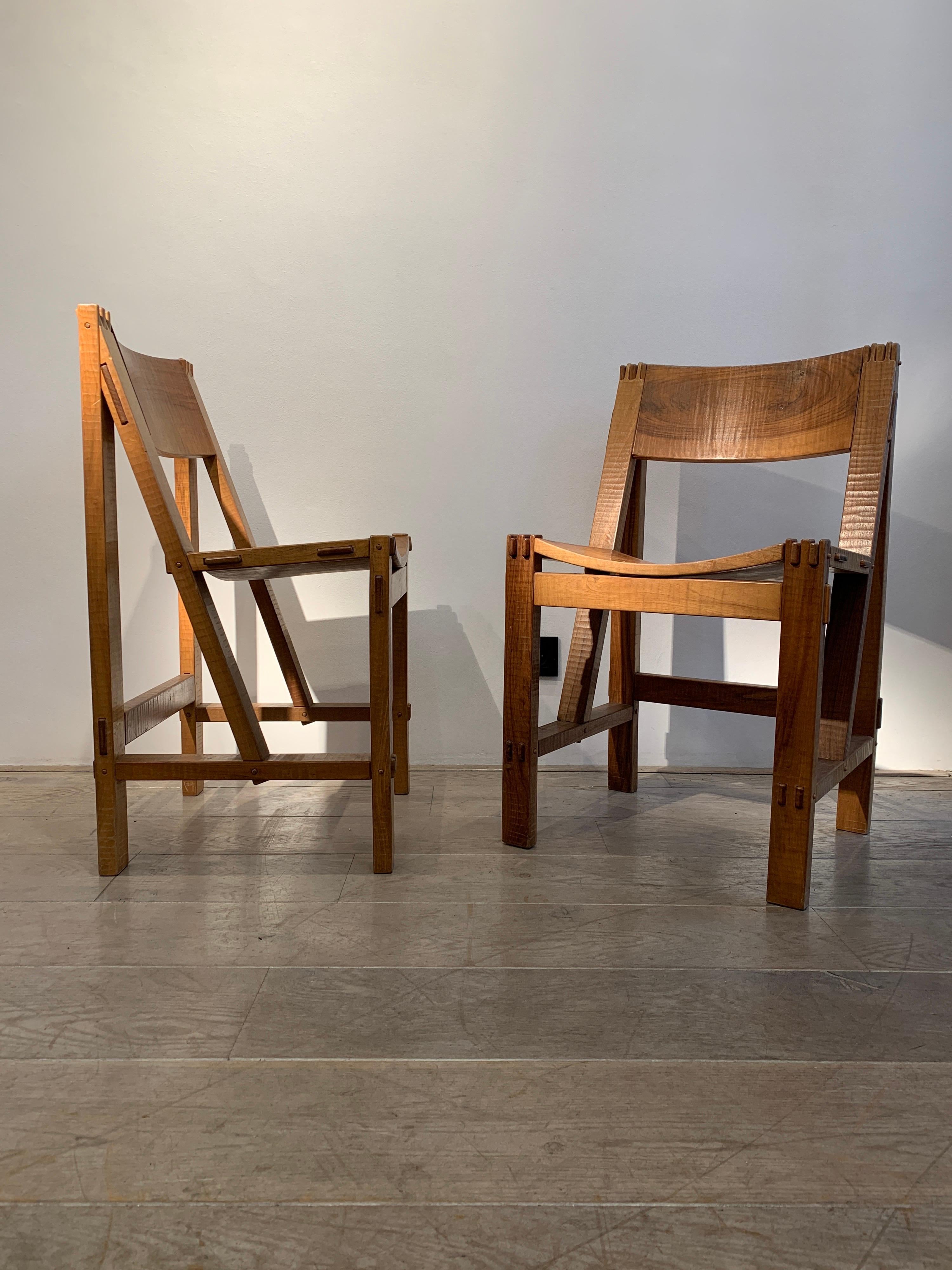 The pair is by Giuseppe Rivadossi. The model is known as the Regina chair. It was designed in 1962 and realized from 1968. The set dates circa 1968-1970s. It is totally handmade in Italian walnut. The architonic style creates emphasis on the
