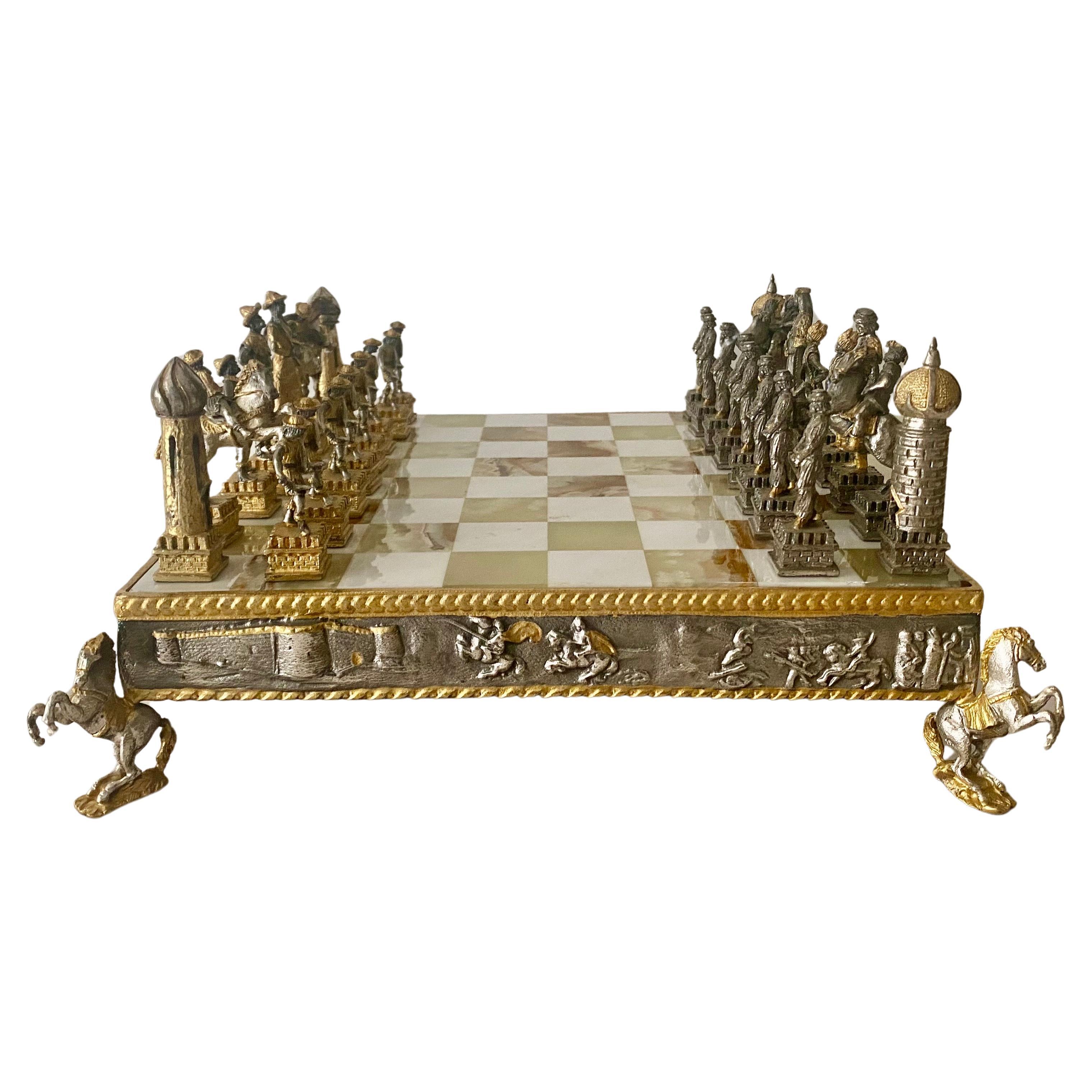 Giuseppe Vasari (1934-2005, Italy), gilt and silvered metal chess set . 
2 tone green and white checked onyx playing surface with relief decorated apron with battle scene panels and stands on figural horse at the corners. All the Figures are signed