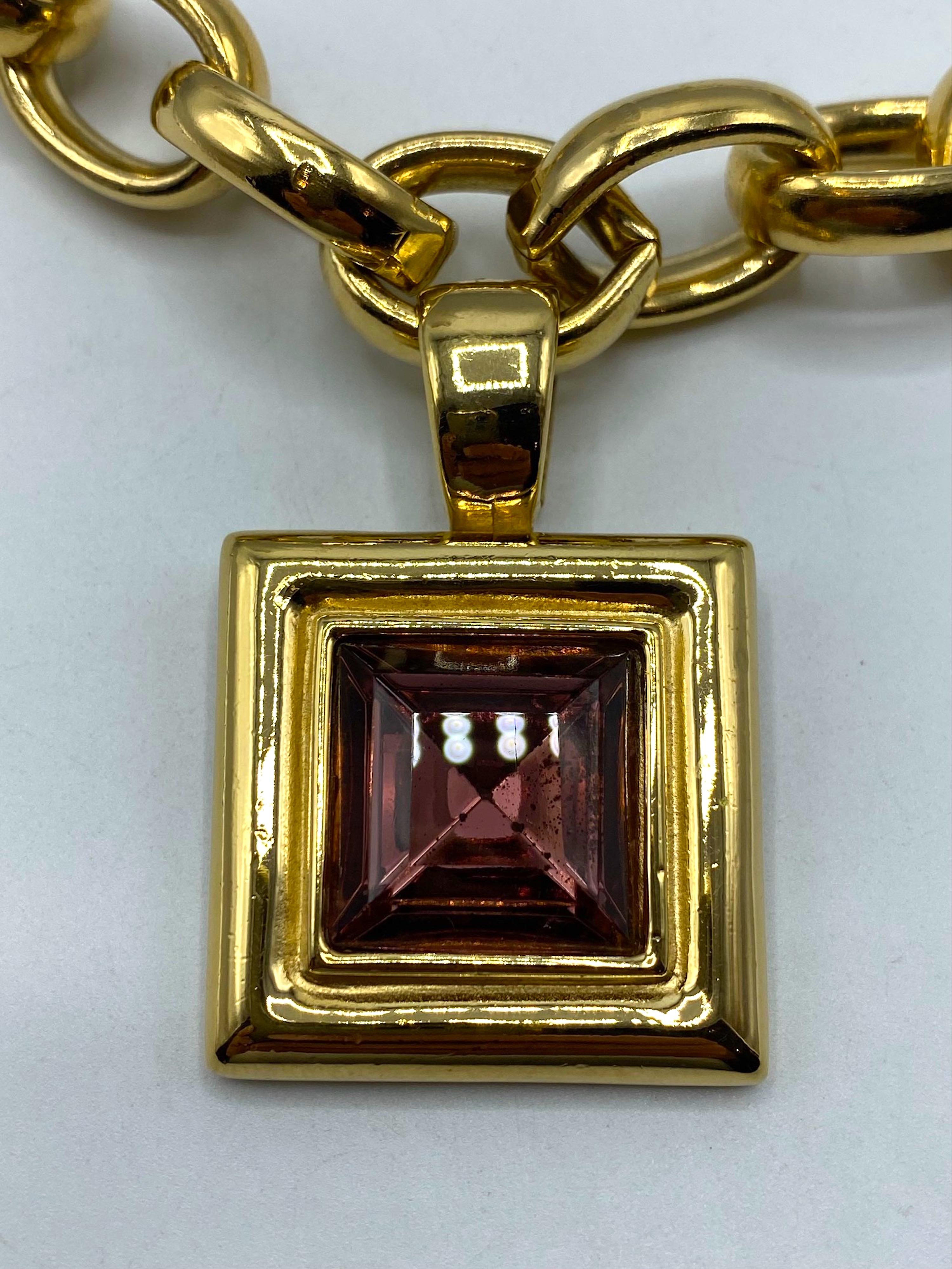 This vintage Givenchy necklace from the 1980s features a bold and statement-making design. The half in wide gold tone large oval link chain adds a touch of glamour, while the 1.5 inch square pendant with a large purple crystal rhinestone adds a pop
