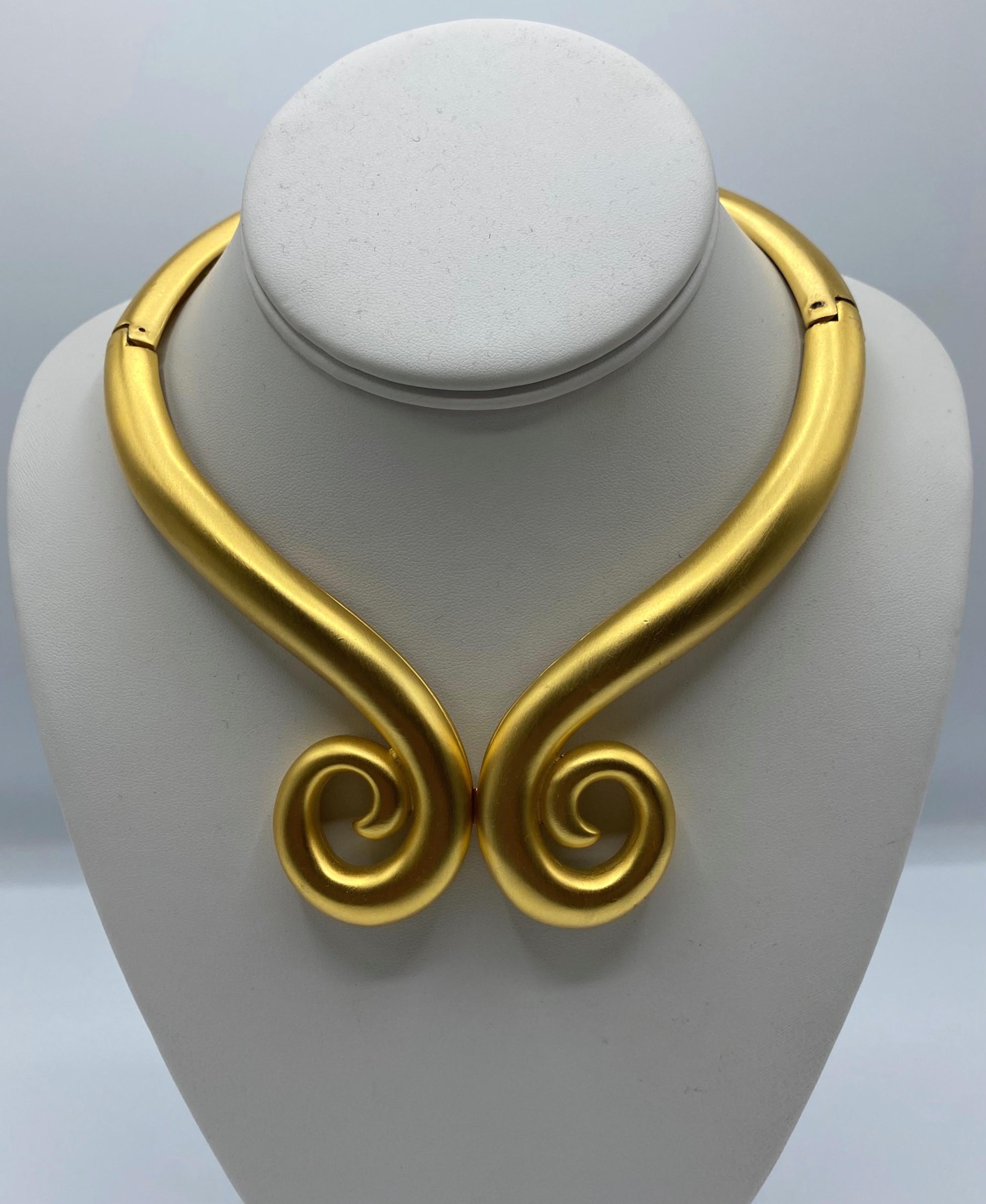 This vintage Givenchy torque necklace is a stunning piece from the 1980s, featuring an elegant satin gold finish with a scroll ribbon design. The front scrolls measure 2.75 inches wide and the necklace has a 15-inch circumference.

It is designed