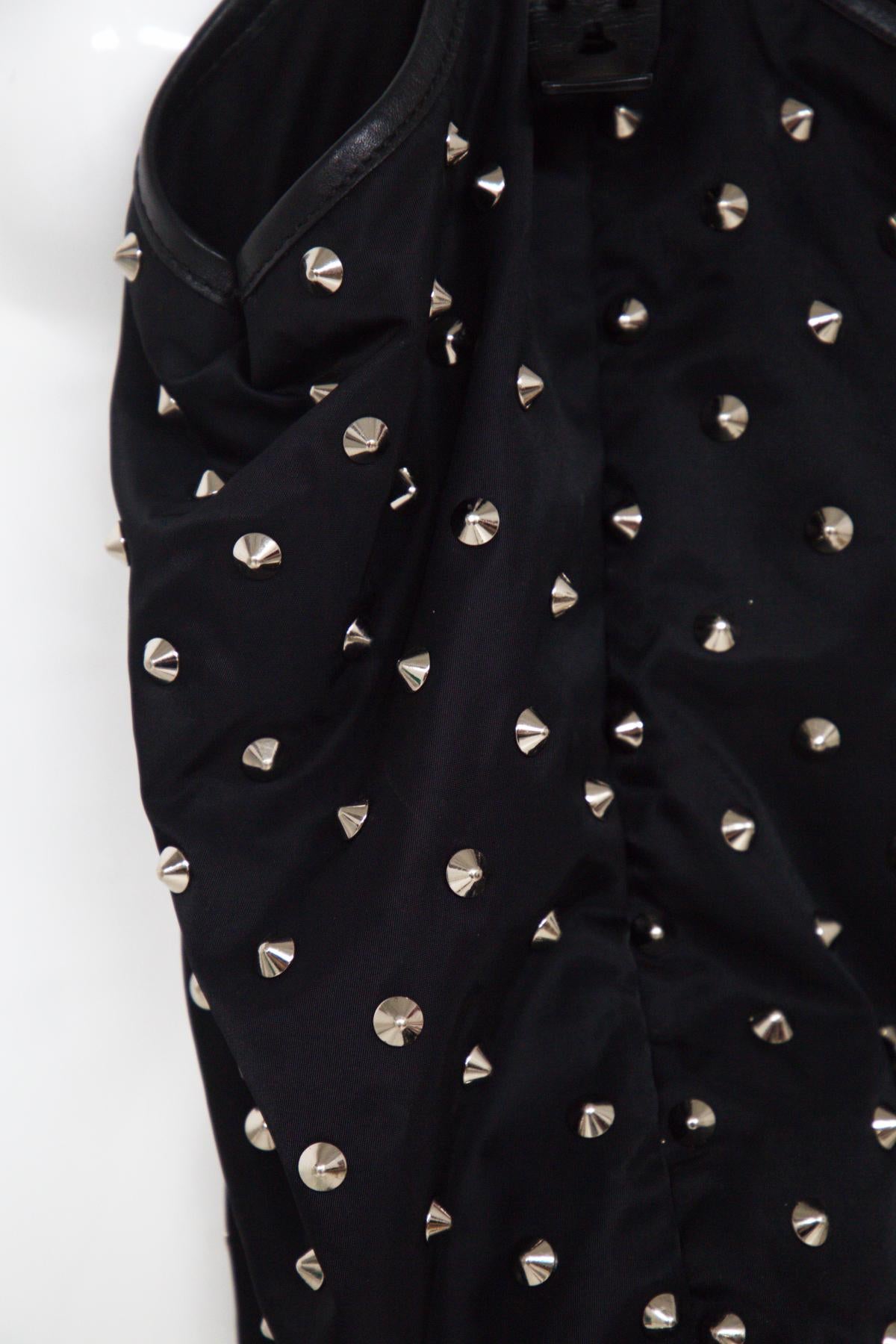 Superbe sac noir Givenchy des années 2000.
Le sac se compose d'un corps en nylon noir orné de clous argentés, de poignées en cuir plat brillant, d'une fermeture à bouton-pression magnétique sur le dessus et de poches intérieures zippées et à