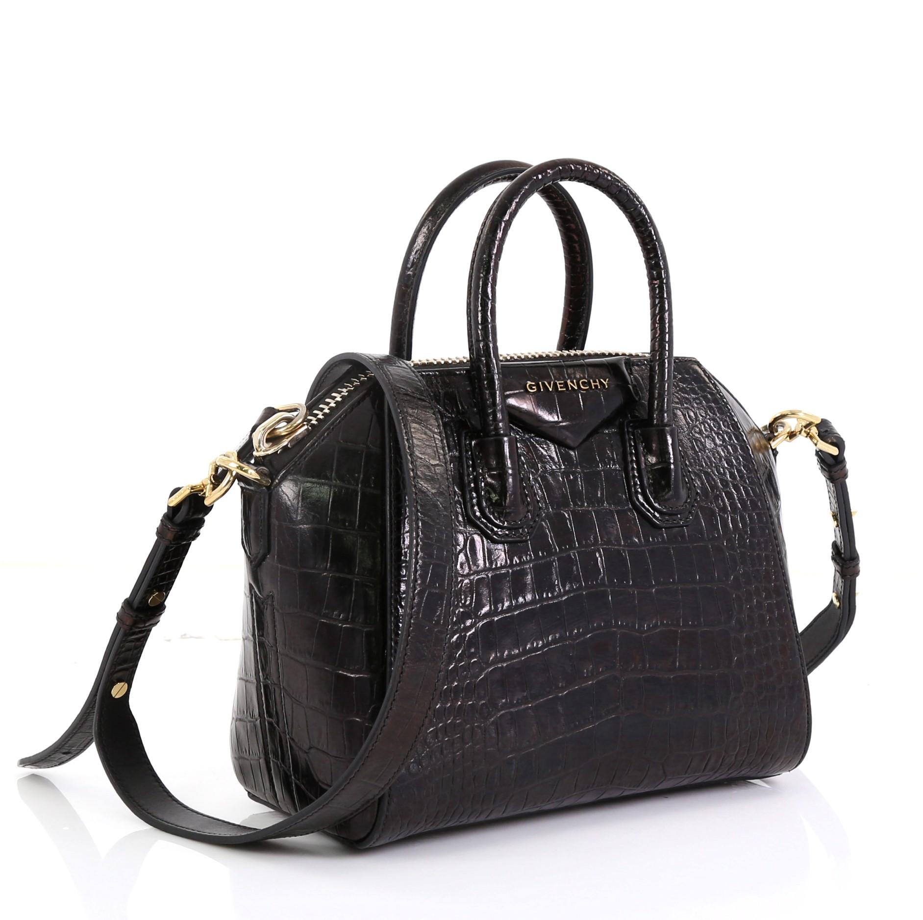This Givenchy Antigona Bag Crocodile Embossed Leather Mini, crafted from black crocodile embossed leather, features dual rolled leather handles and gold-tone hardware. Its zip closure opens to a black fabric interior with zip and slip pockets.