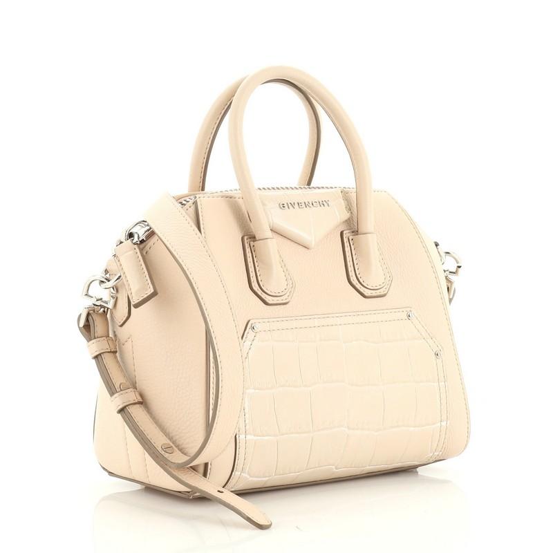 This Givenchy Antigona Bag Leather and Crocodile Embossed Leather Minii, crafted from neutral leather, features dual rolled leather handles and silver-tone hardware. Its zip closure opens to a neutral fabric interior with zip and slip pockets.