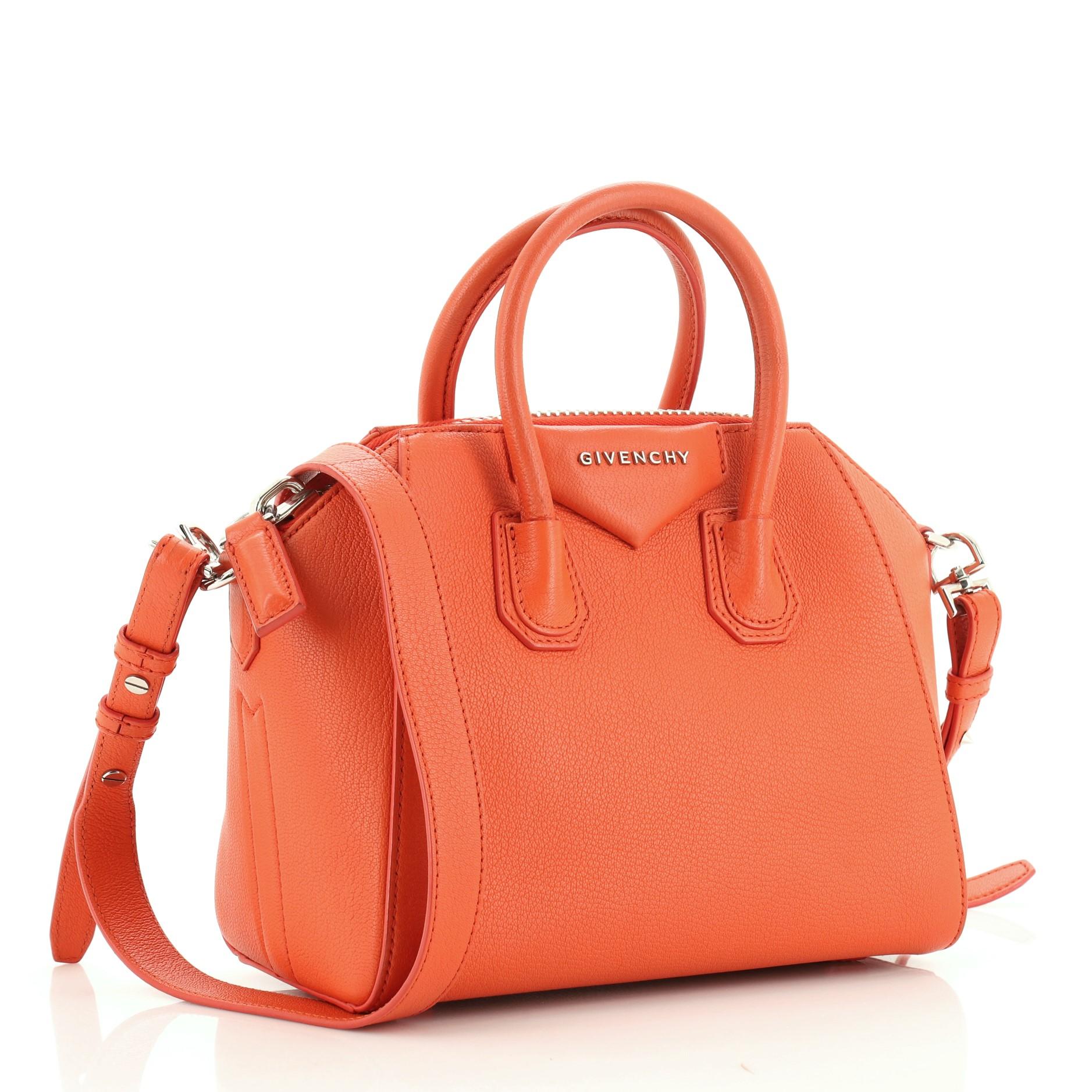 This Givenchy Antigona Bag Leather Mini, crafted from orange leather, features dual rolled leather handles and silver-tone hardware. Its zip closure opens to a neutral fabric interior with zip and slip pockets. These are professional pictures of the