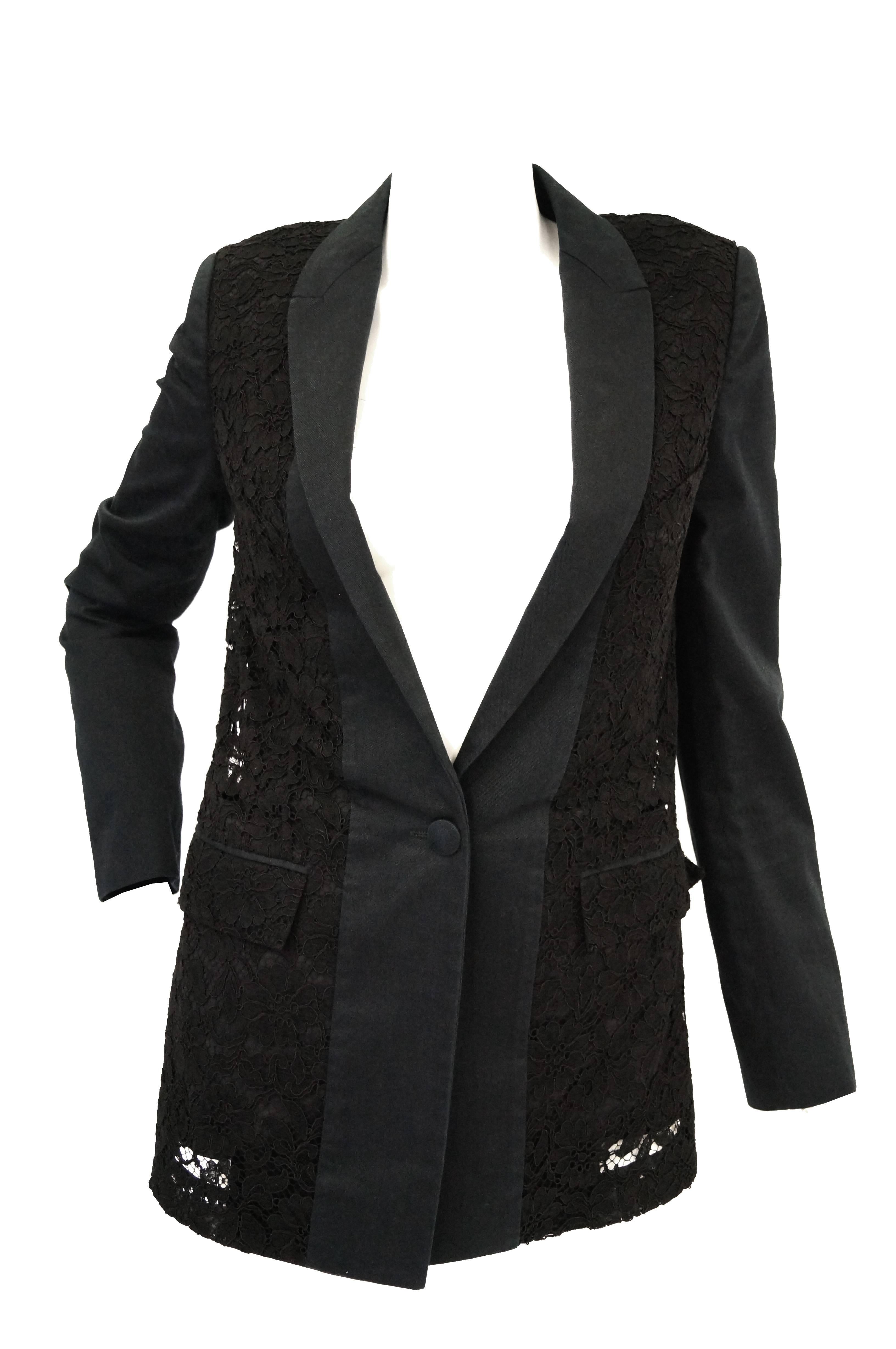 Gorgeous black lace thin lapel longline blazer by Hubert de Givenchy. The blazer features long sleeves, a low neckline with narrow solid black lapels, two pockets, and hit at the waist. The blazer has structured shoulders, and a single button