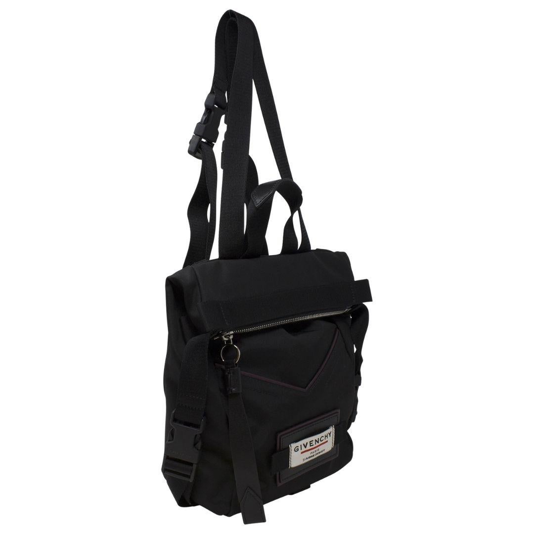 This cutting edge and super street style backpack is crafted in durable black nylon. This backpack features adjustable nylon shoulder straps, a small top handle, and silver hardware throughout. The top zipper opens to a spacious black nylon interior