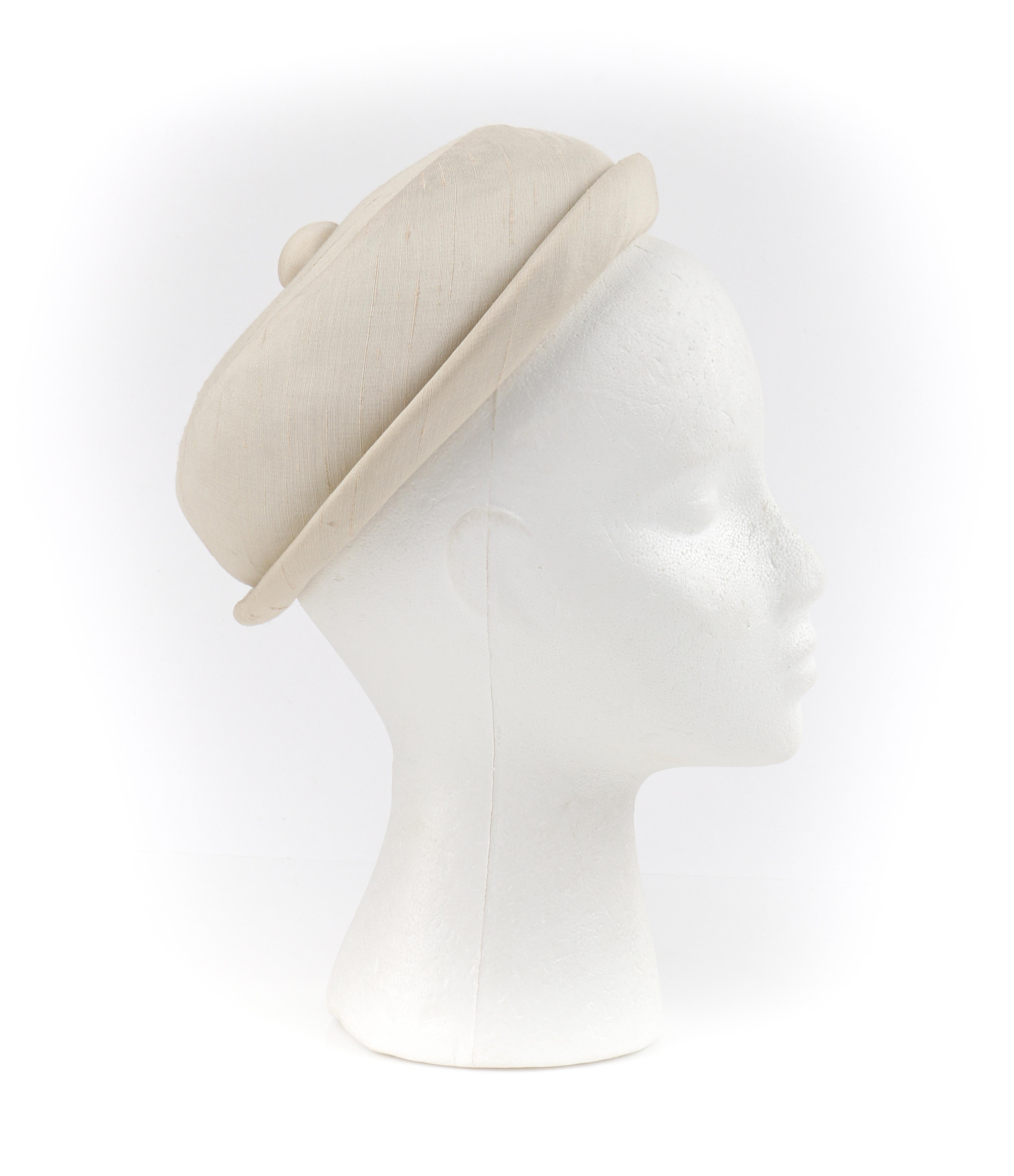 GIVENCHY c.1950's Solid Cream Silk Duponi Pillbox Style Detailed Button Top Hat

Circa: 1950’s 
Label(s): HUBERT de GIVENCHY PARIS; Saks Fifth Avenue
Style: Pillbox
Color(s): Cream
Lined: Yes 
Unmarked Fabric Content (feel of): Exterior: Silk Duponi