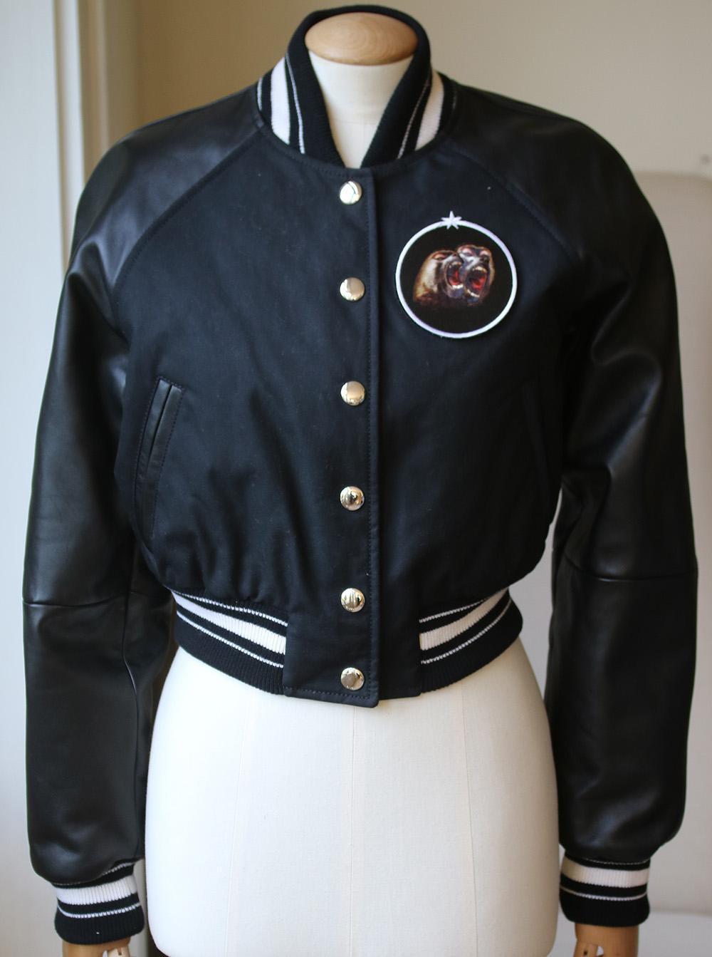 This black cotton, lambskin and wool cropped bomber jacket from Givenchy features a ribbed collar, a snap button closure, long length raglan sleeves, two slanted front pockets, a ribbed hem and cuffs, a full lining, a white striped trim and a