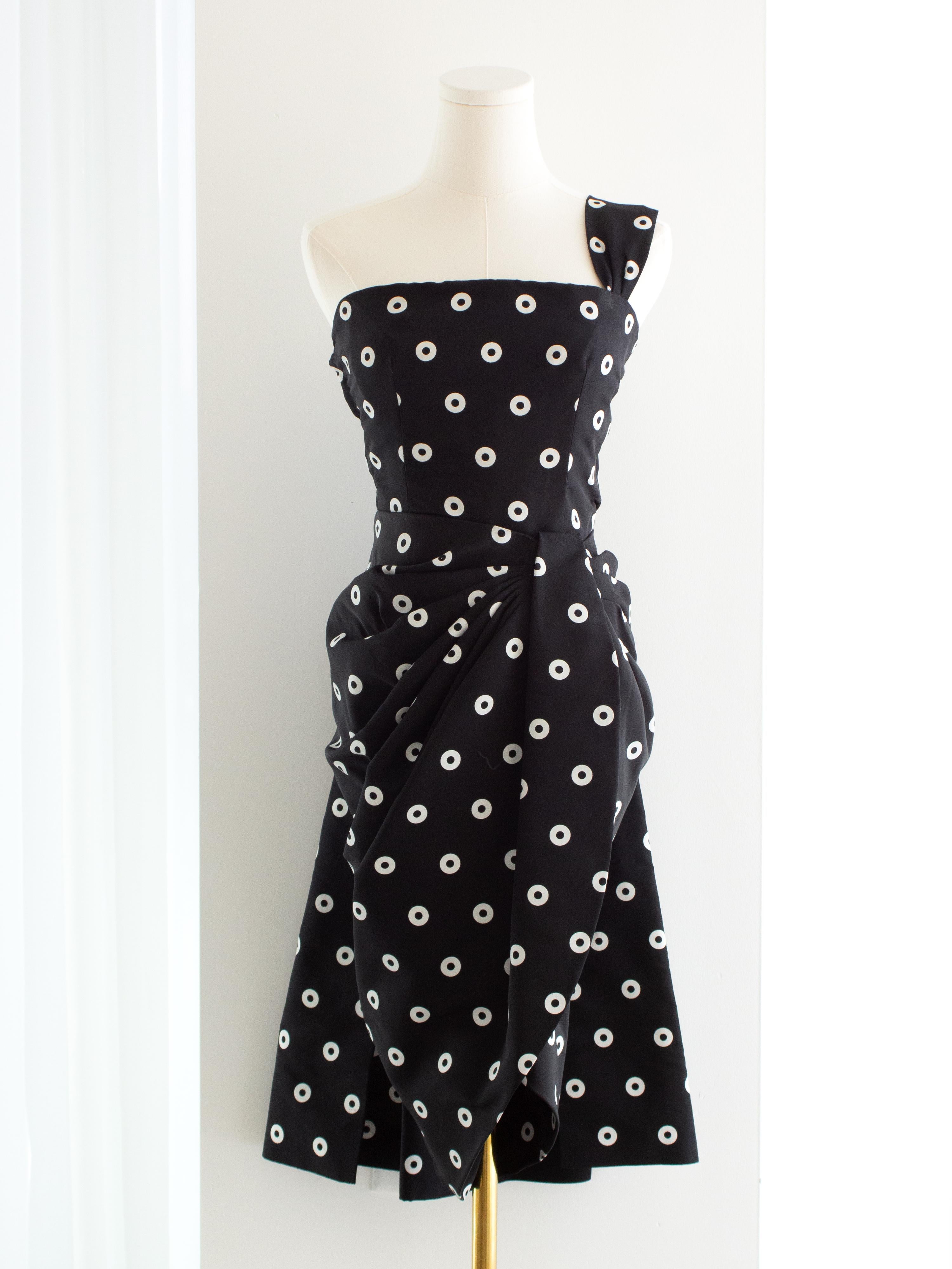 Este impresionante vestido vintage Givenchy de finales de los 80 desprende elegancia con un toque juguetón. Confeccionado en un lujoso tejido negro adornado con lunares blancos, el vestido presenta un diseño asimétrico de un solo hombro, que añade